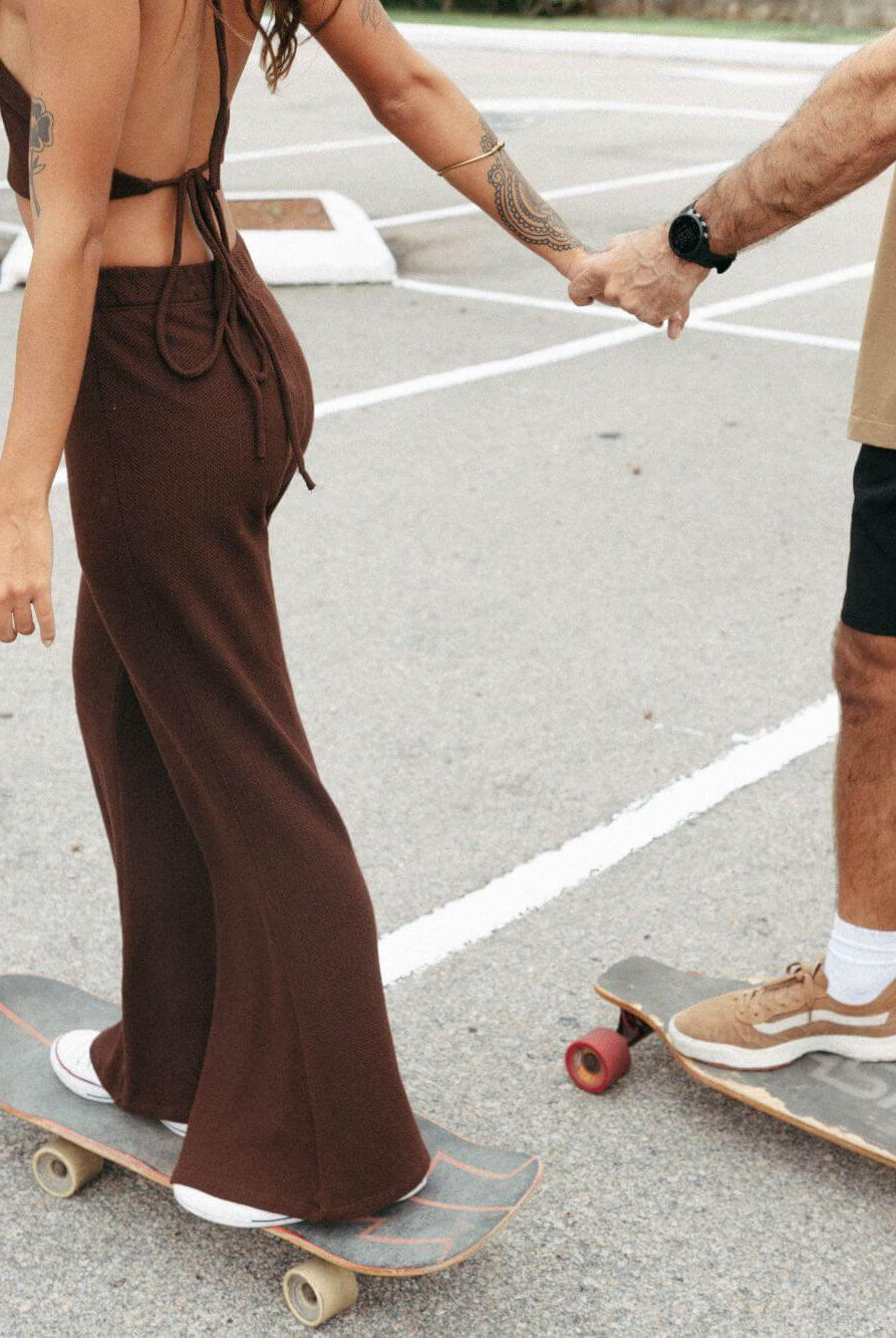 Casal andando de skate, mulher usando calça tricot Ker chocolate da Greenish, look confortável e estiloso.