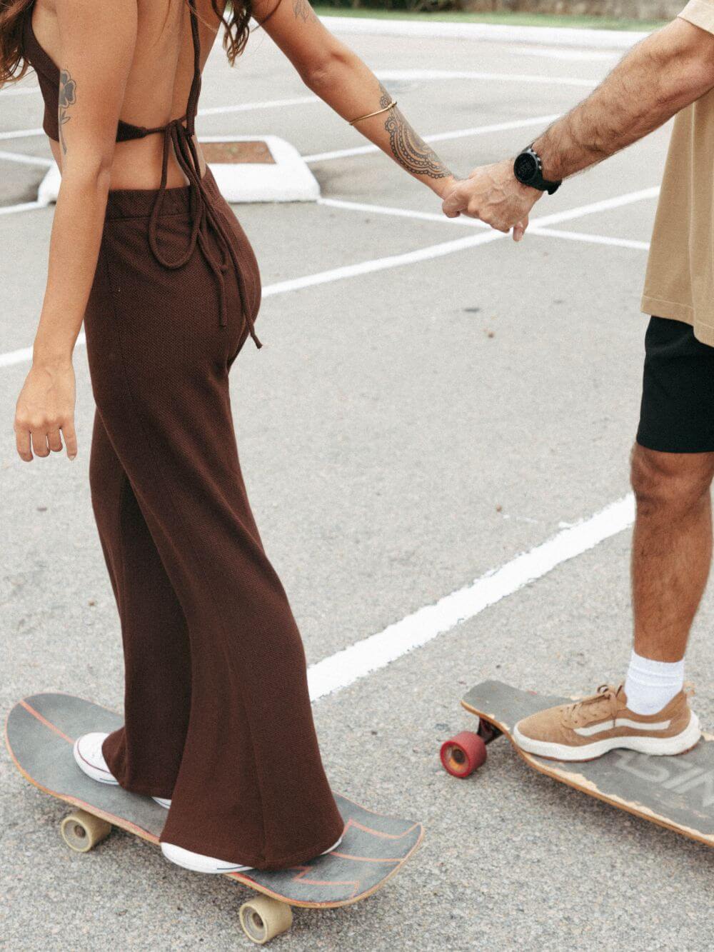Casal andando de skate, mulher usando calça tricot Ker chocolate da Greenish, look confortável e estiloso.