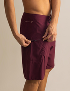 Homem vestindo boardshort Total Stretch Bordo da Greenish, mostrando bolso lateral. Tecido elástico e secagem rápida para surfistas.