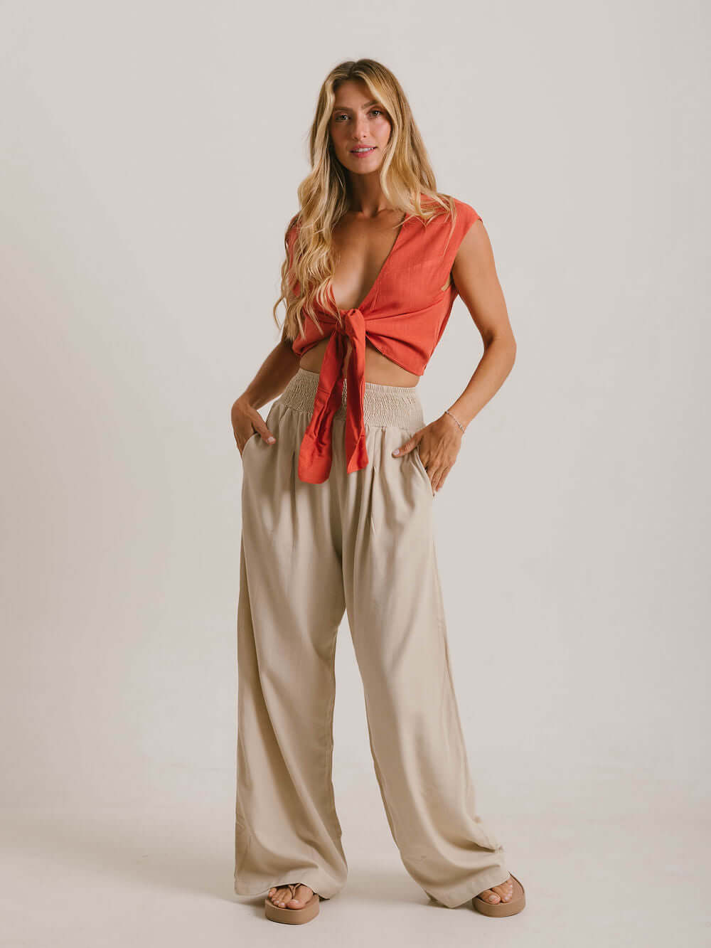 Blusa Ruth da Greenish na cor laranja, com amarração frontal e tecido leve, combinando com calça bege.