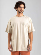 Camiseta oversized masculina Greenish, modelo em tom areia com estampa original, ideal para looks streetwear.