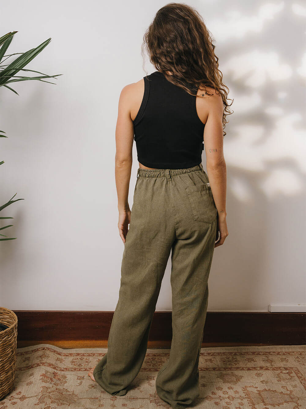 Mulher usando calça linho verde Khay da marca Greenish, vista de costas, perfeita para looks casuais.