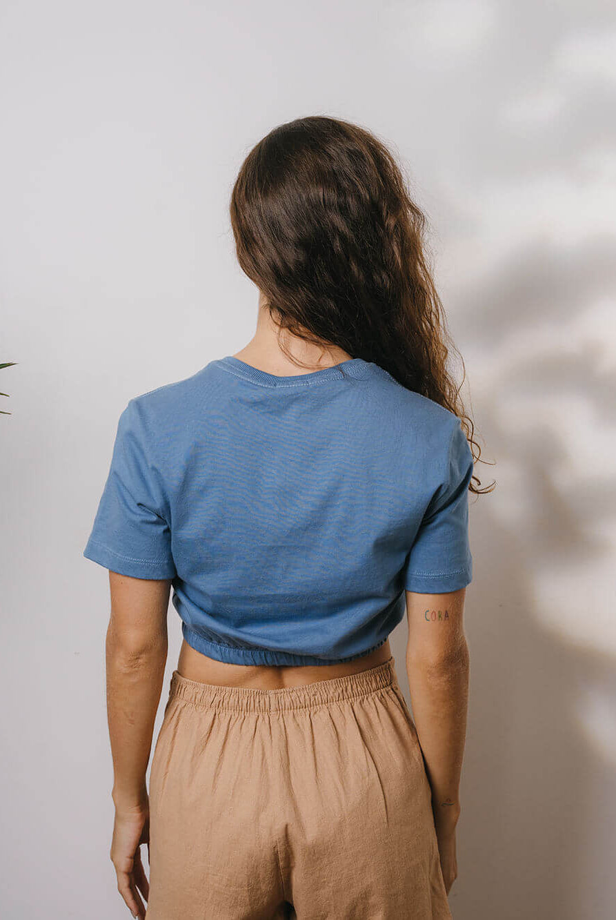 Blusa Sally azul médio da Greenish vista de trás em modelo com calça clara.