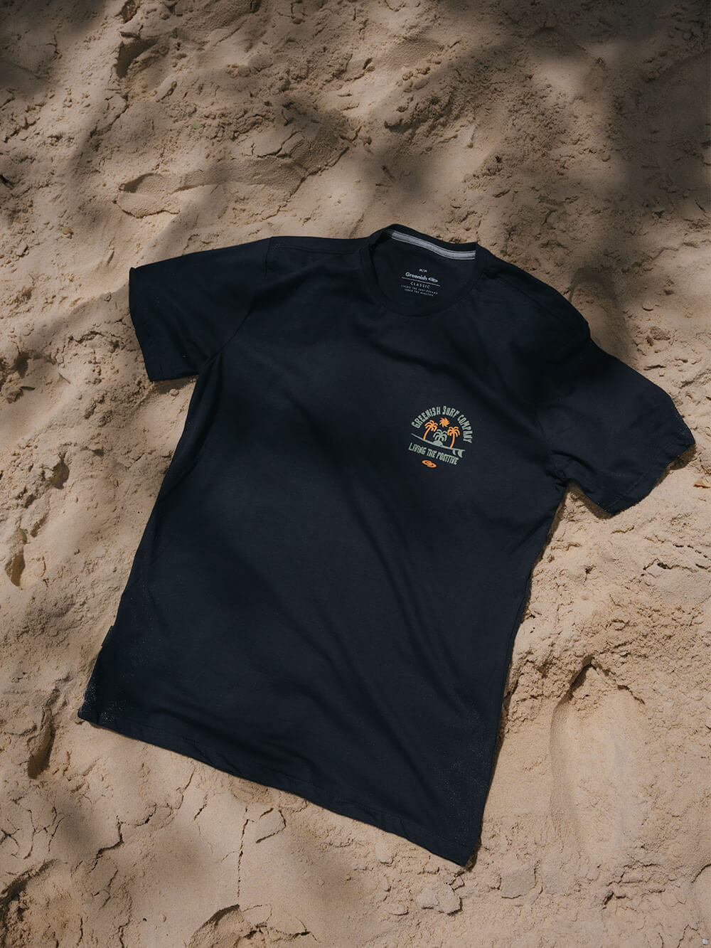 Camiseta Living The Positive azul marinho da marca Greenish, estampa animada sobre fundo de areia.