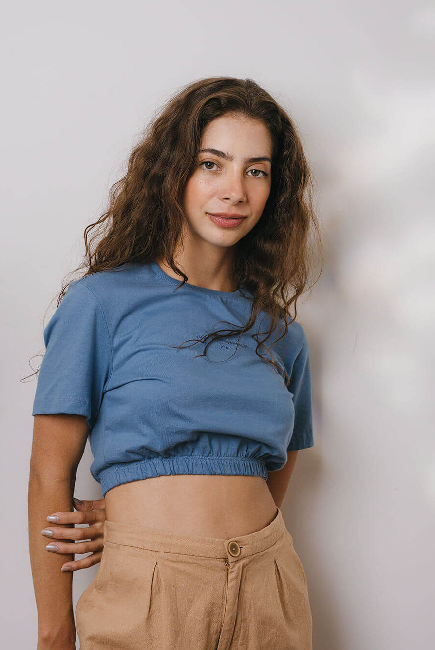 Modelo vestindo blusa Sally azul médio da marca Greenish, com detalhe franzido na cintura.