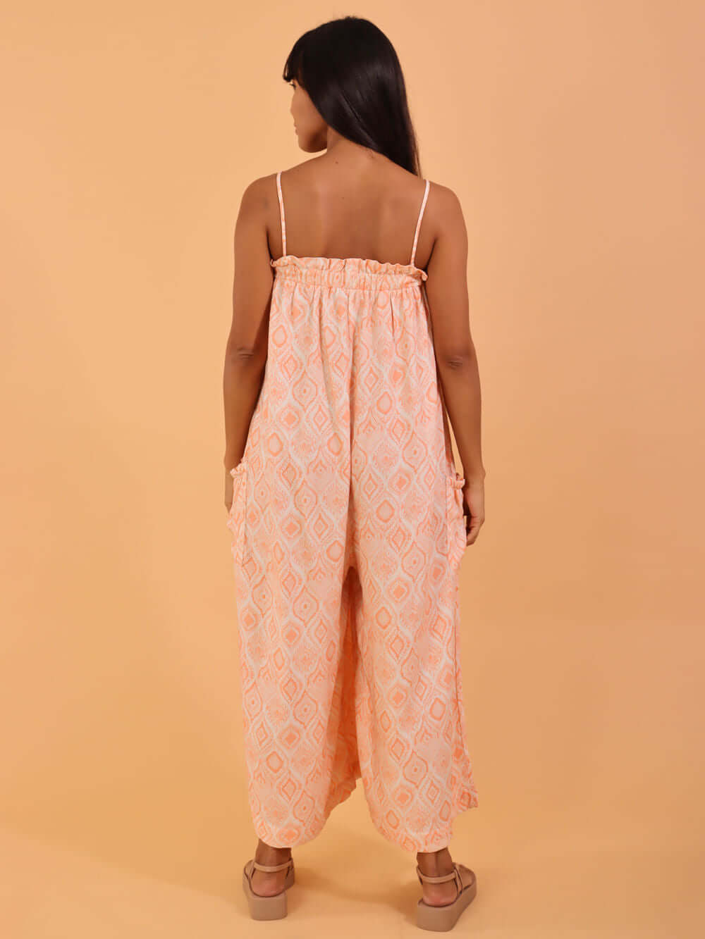 Macacão midi Emily da Greenish na cor coral, sendo exibido de costas em fundo laranja.