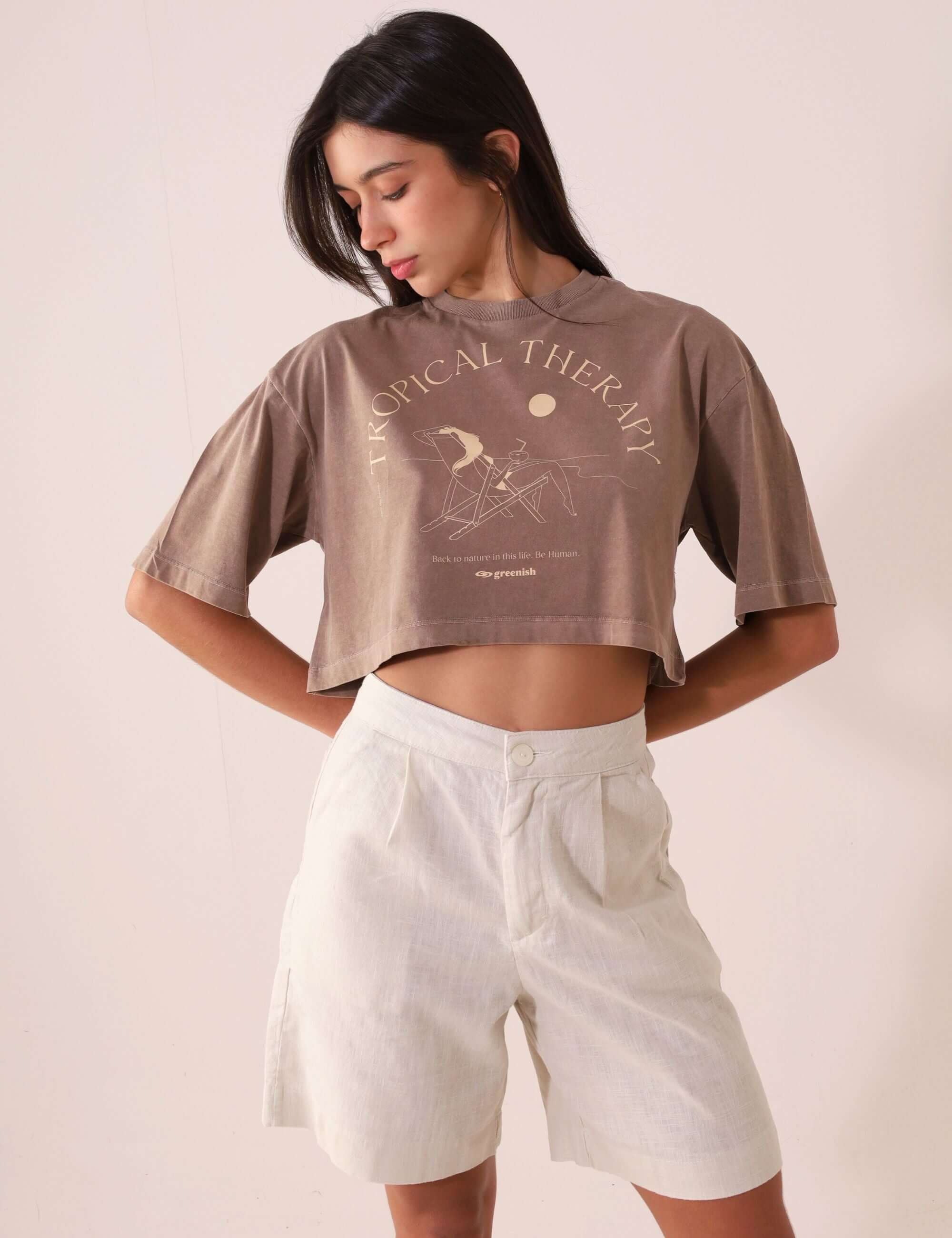 Modelo vestindo SHORT CLARA - AREIA com camiseta cropped marrom, Greenish, bermuda feminina em tecido leve e respirável, estilo alfaiataria.