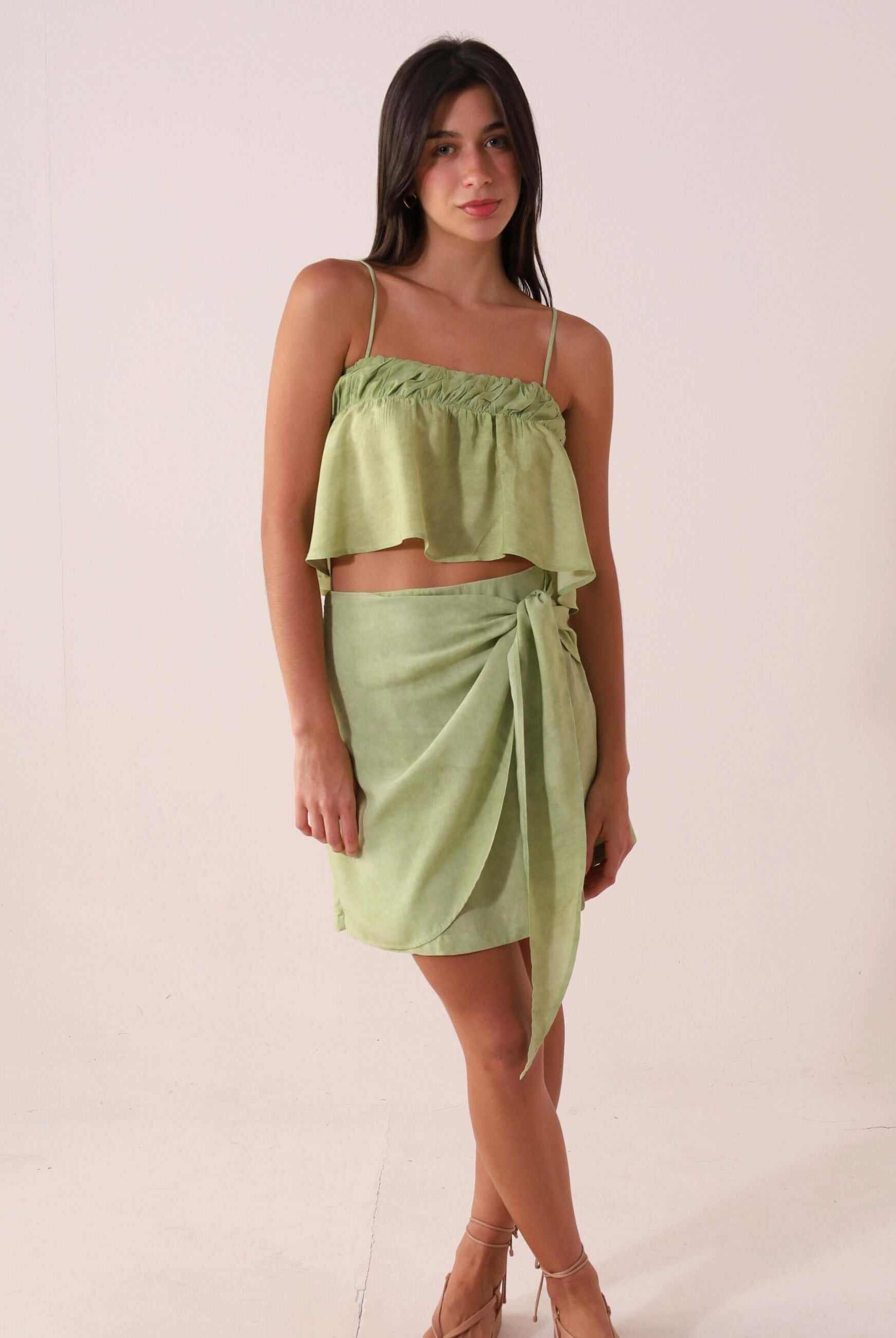 Mulher vestindo SAIA CURTA THÁ - VERDE da Greenish, feita de viscose com cintura alta e amarração lateral, destacando visual elegante.