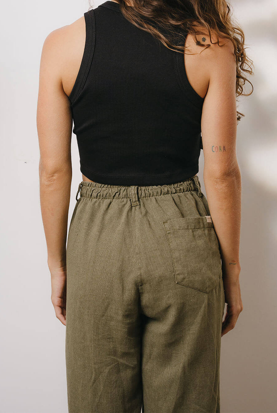 Mulher usando calça linho Khay verde da marca Greenish, com cós elástico e corte reto, vista de trás.