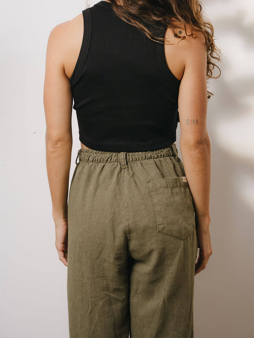 Mulher usando calça linho Khay verde da marca Greenish, com cós elástico e corte reto, vista de trás.