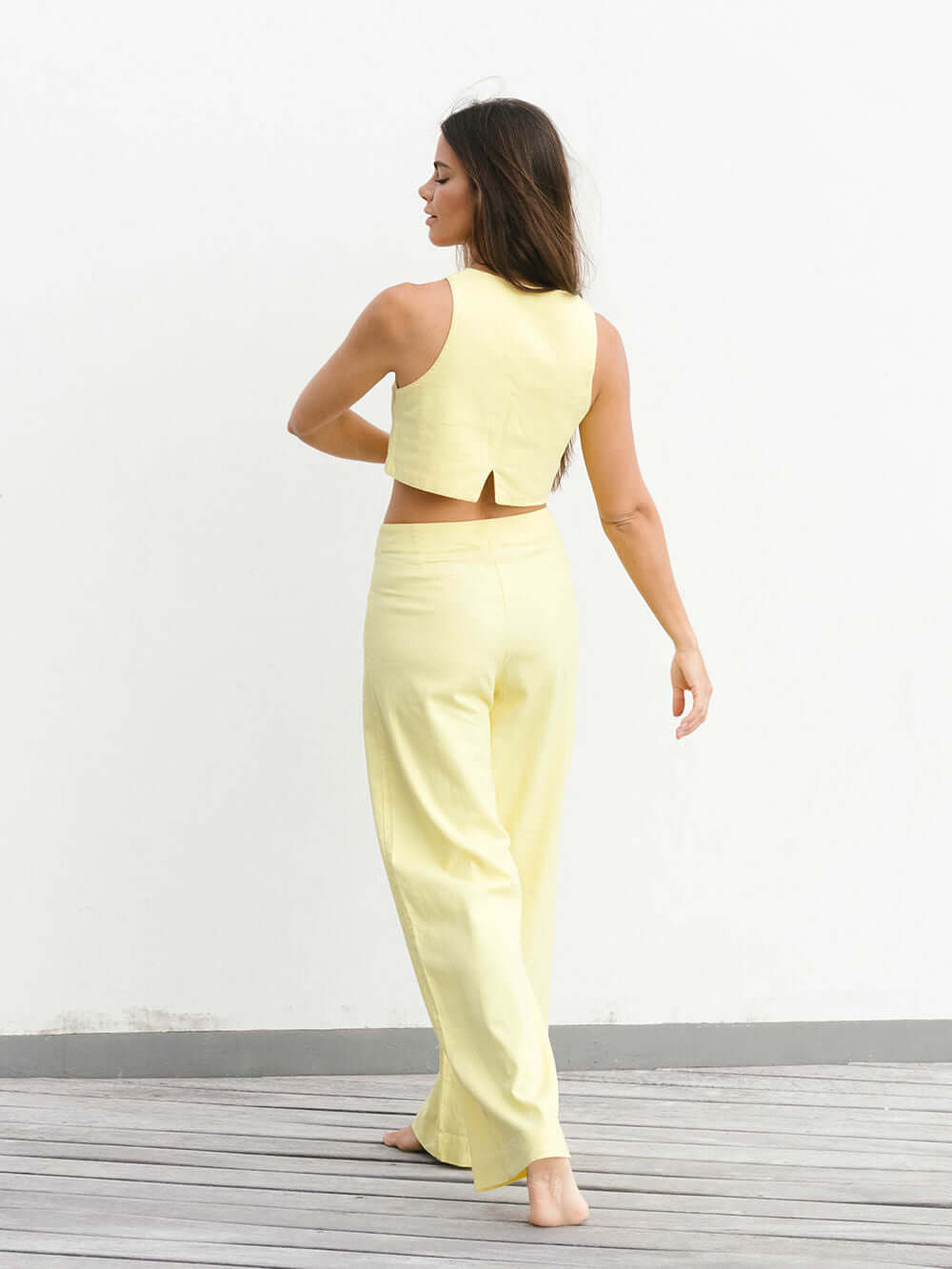 Modelo de costas usando calça Hazel amarela da marca Greenish, com caimento solto e estilo vintage.