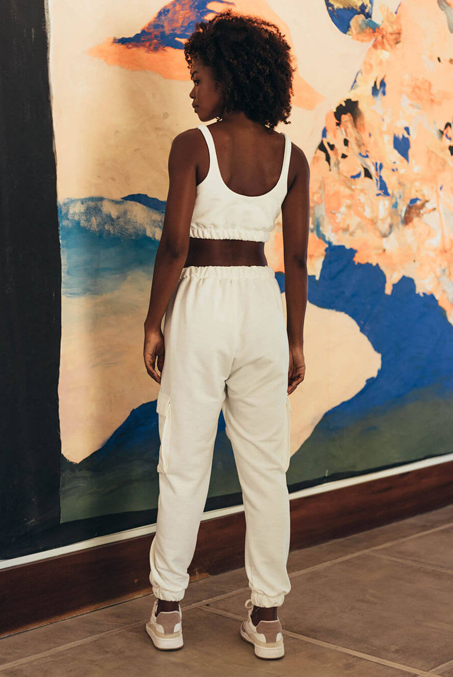 Modelo usando calça moletom Jucca branca, vista traseira, em ambiente artístico. Marca: Greenish.