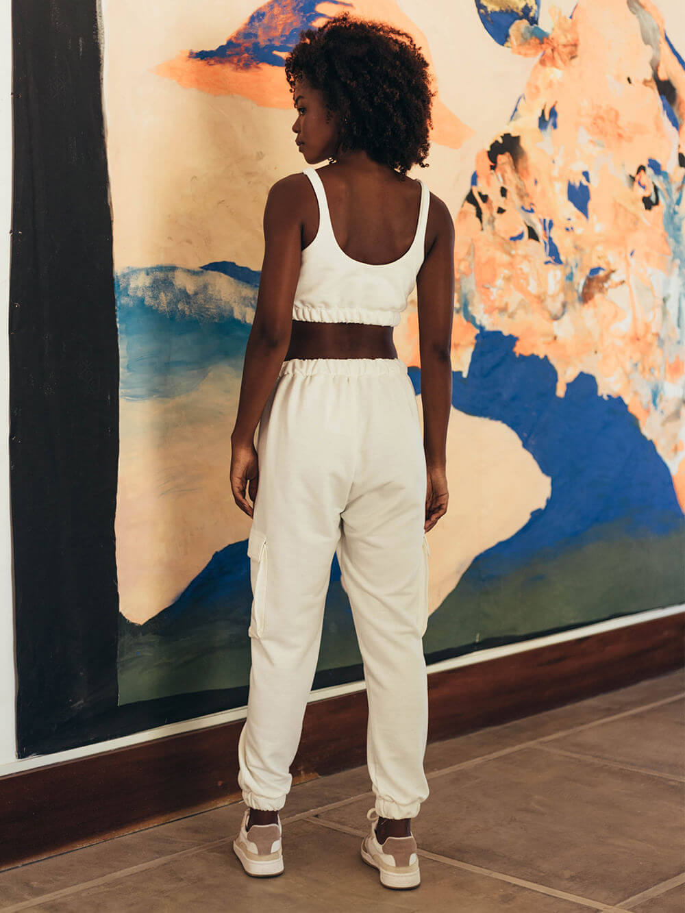 Modelo usando calça moletom Jucca branca, vista traseira, em ambiente artístico. Marca: Greenish.