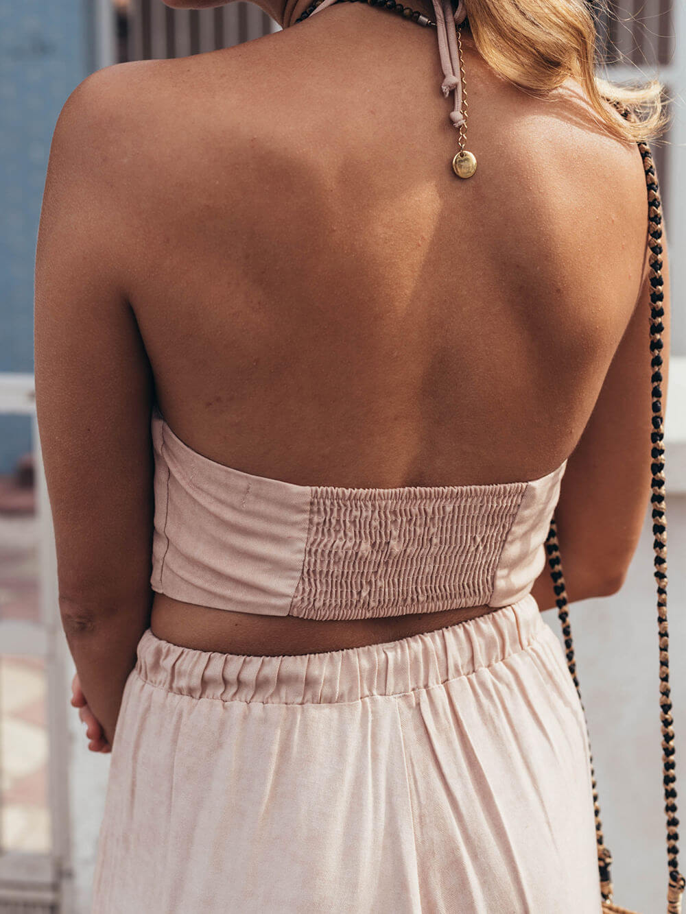 Blusa cropped Cecília bege da Greenish, vista pela parte de trás, com detalhe de lastex e amarração no pescoço.