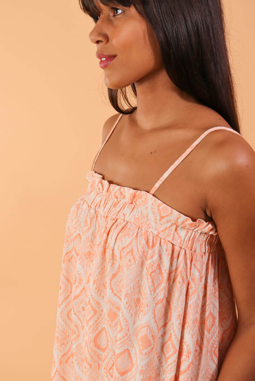 Modelo usando macacão midi Emily da Greenish em coral, destacando detalhes de estampa e alças finas.