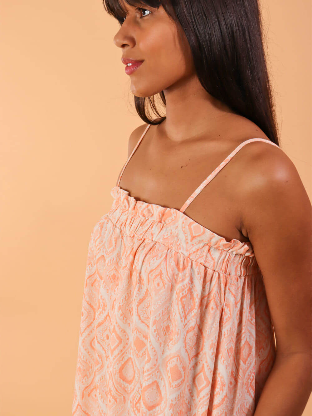 Modelo usando macacão midi Emily da Greenish em coral, destacando detalhes de estampa e alças finas.