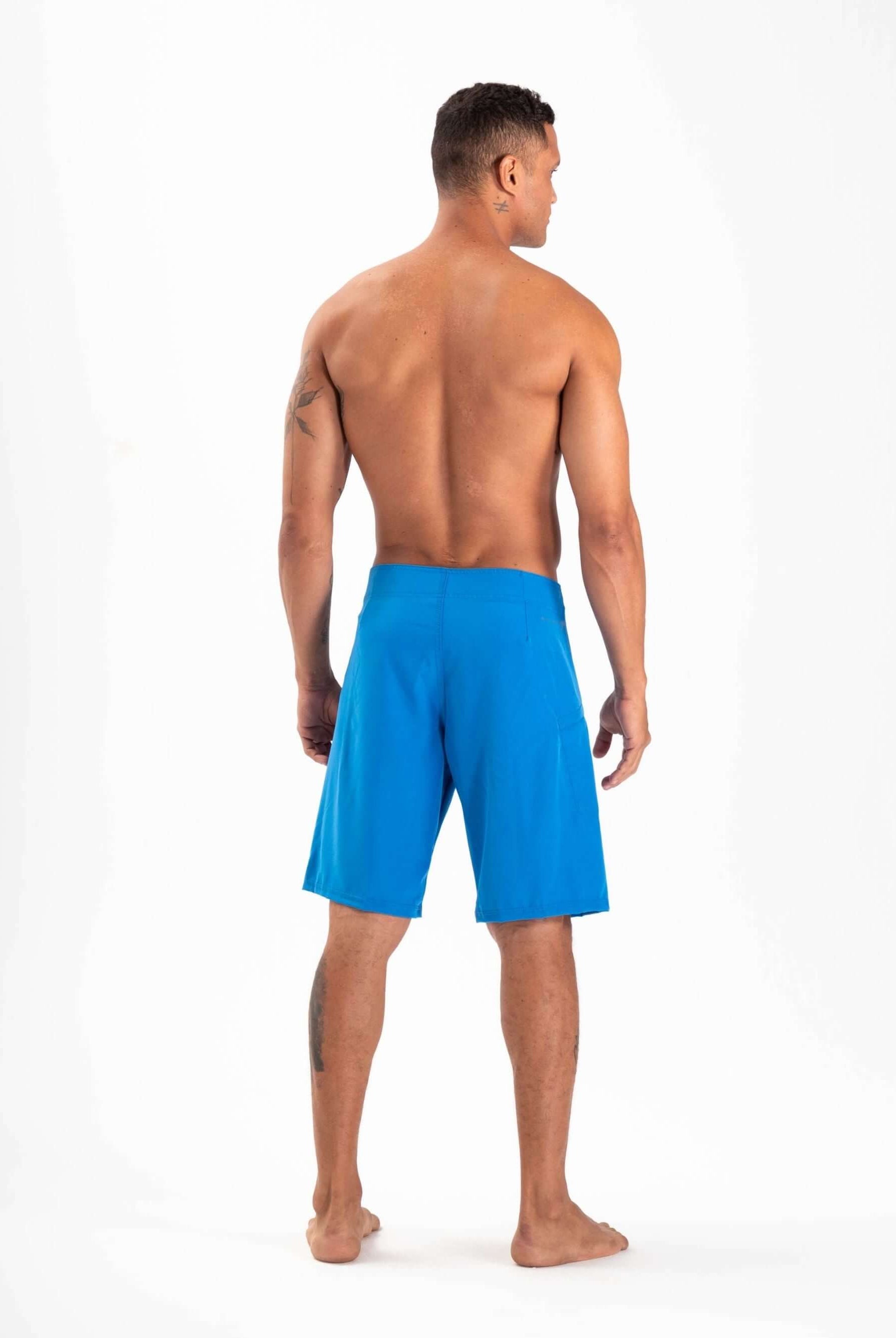 Man wearing Greenish Total Stretch boardshorts in azul, designed for high-performance activities and quick drying.