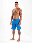 Model wearing Greenish Total Stretch Boardshorts in blue, ideal for high-performance water sports.
