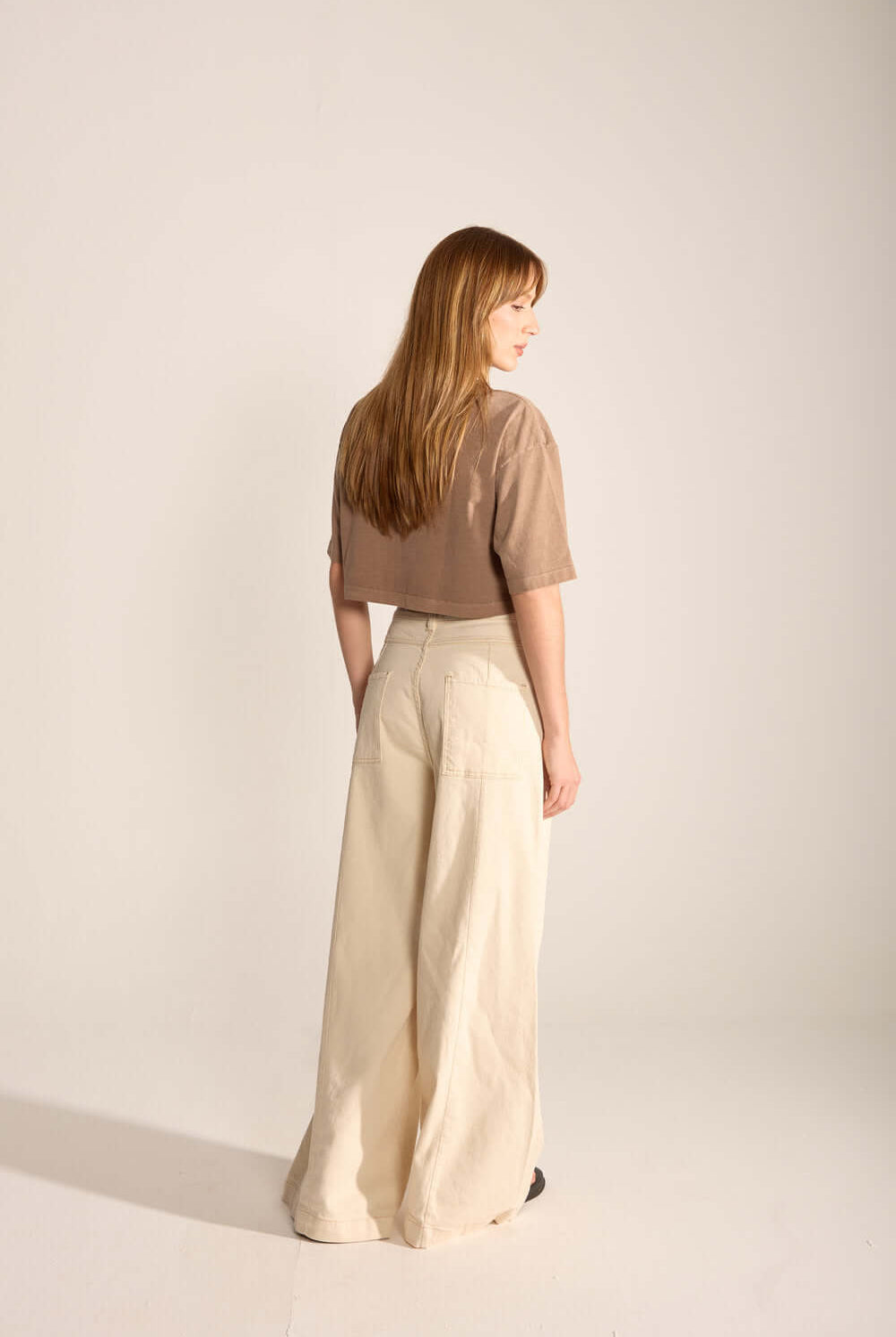 Modelo usando a Calça Laila da Greenish, estilo wide leg, em fundo neutro, mostrando recortes e conforto contemporâneo.