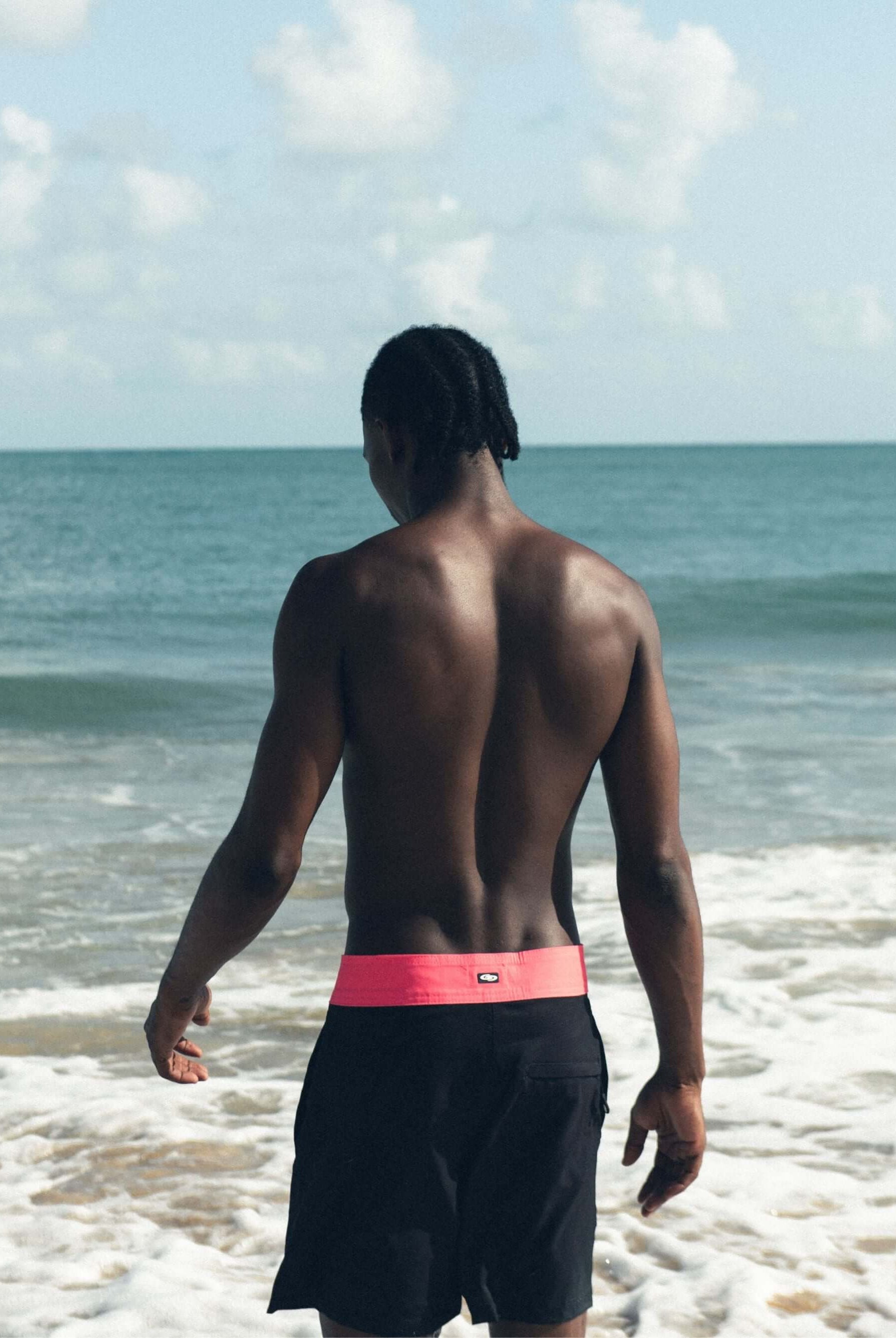 Homem de costas usando bermuda Boardwalk Sunny Viber da Greenish na praia, destacando conforto e estilo.