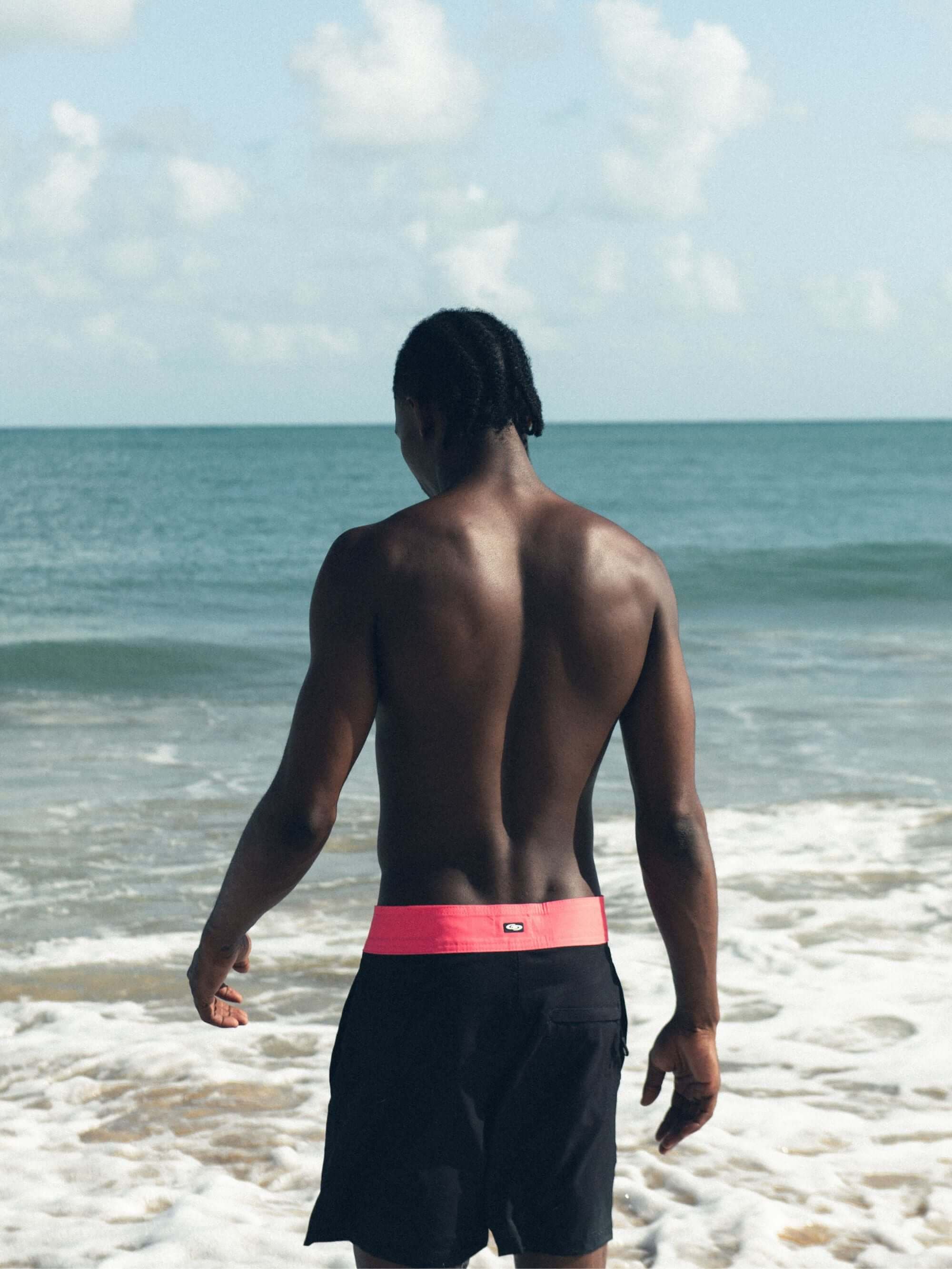 Homem de costas usando bermuda Boardwalk Sunny Viber da Greenish na praia, destacando conforto e estilo.