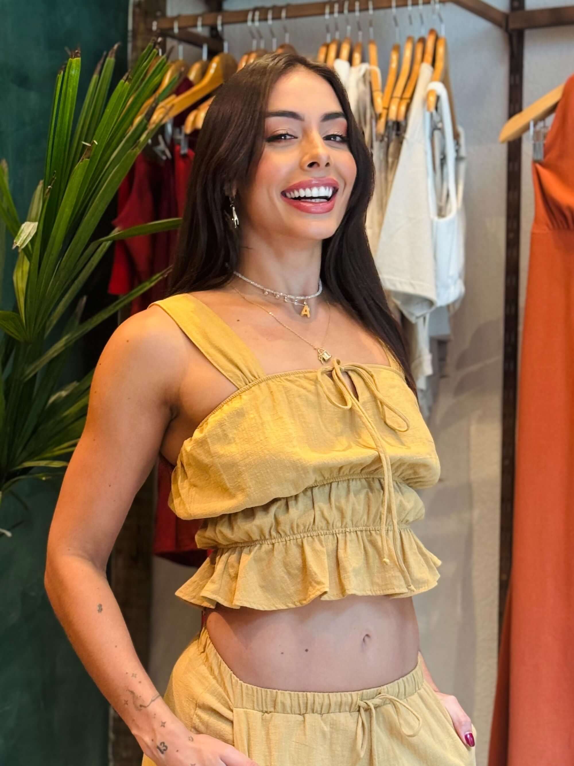 Modelo usando a blusa Marye caqui da Greenish, com detalhes em babados, em ambiente de loja.