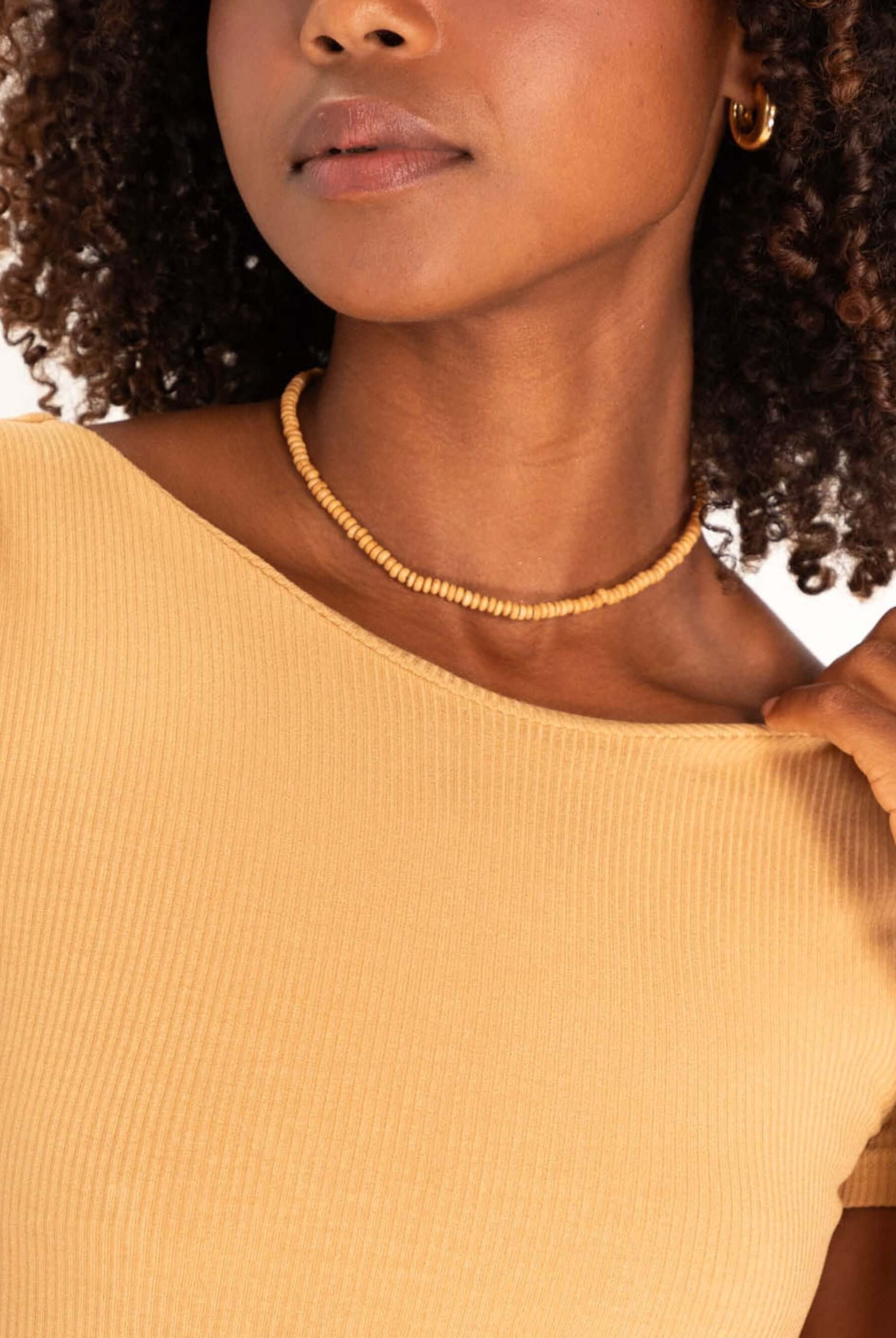 Close-up de mulher com blusa amarelo claro, destacando colar e penteado. Estilo moderno e elegante.