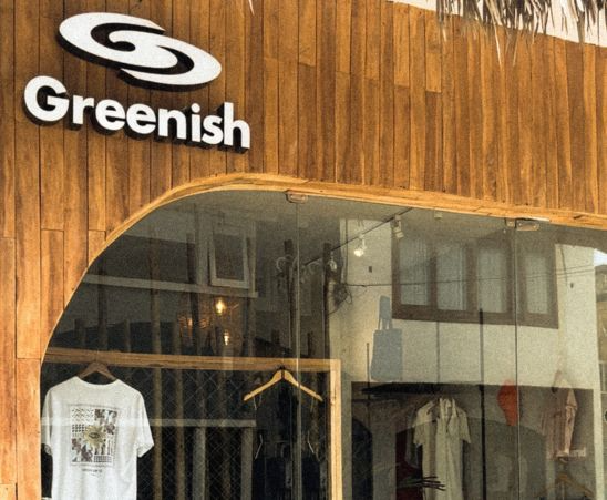 Fachada da loja Greenish com letras em destaque. Roupas expostas em um ambiente acolhedor.