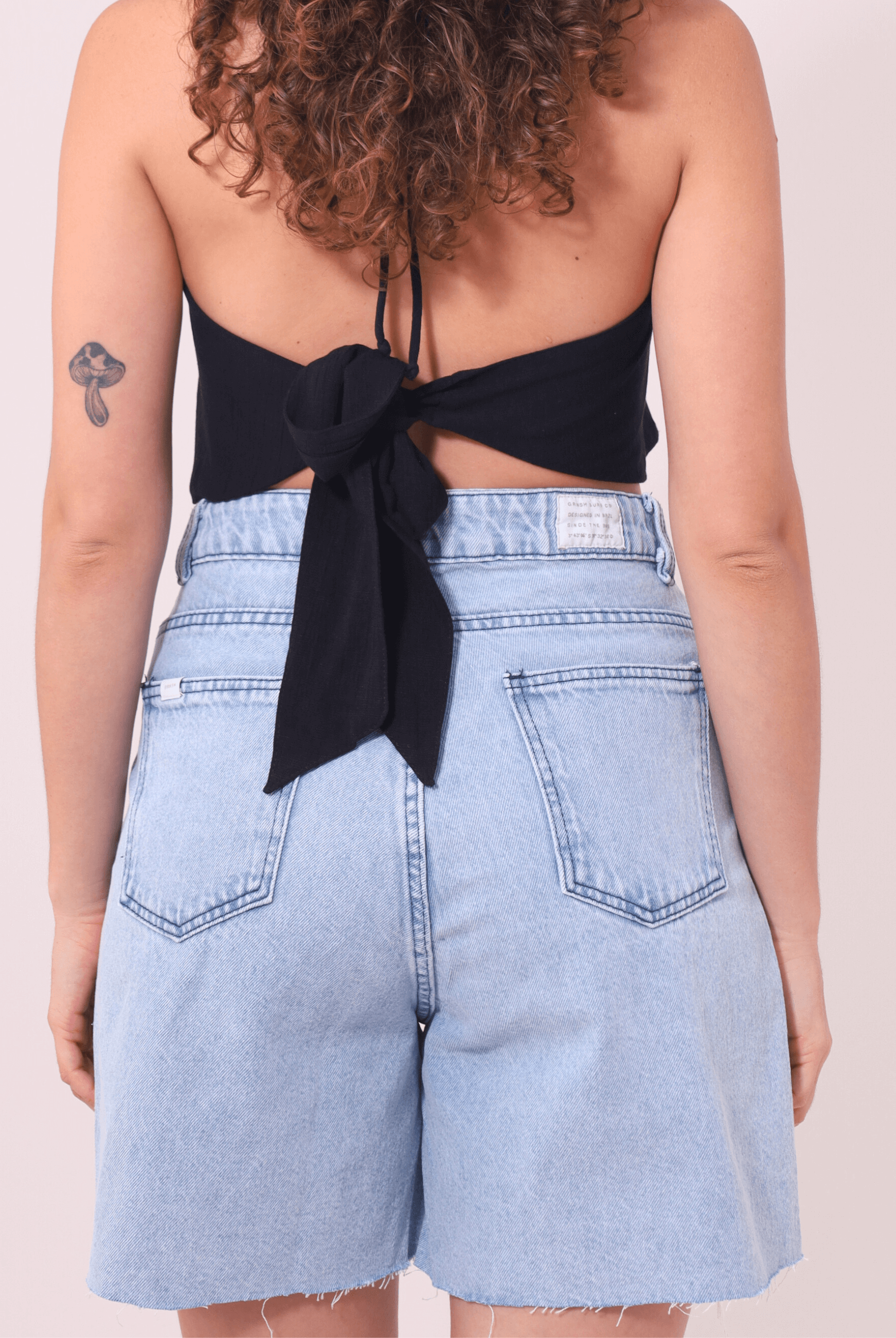 Bermuda Jeans Glicia Greenish cintura alta vintage azul, estilo e conforto para o verão. Modelo feminino de costas com top preto.