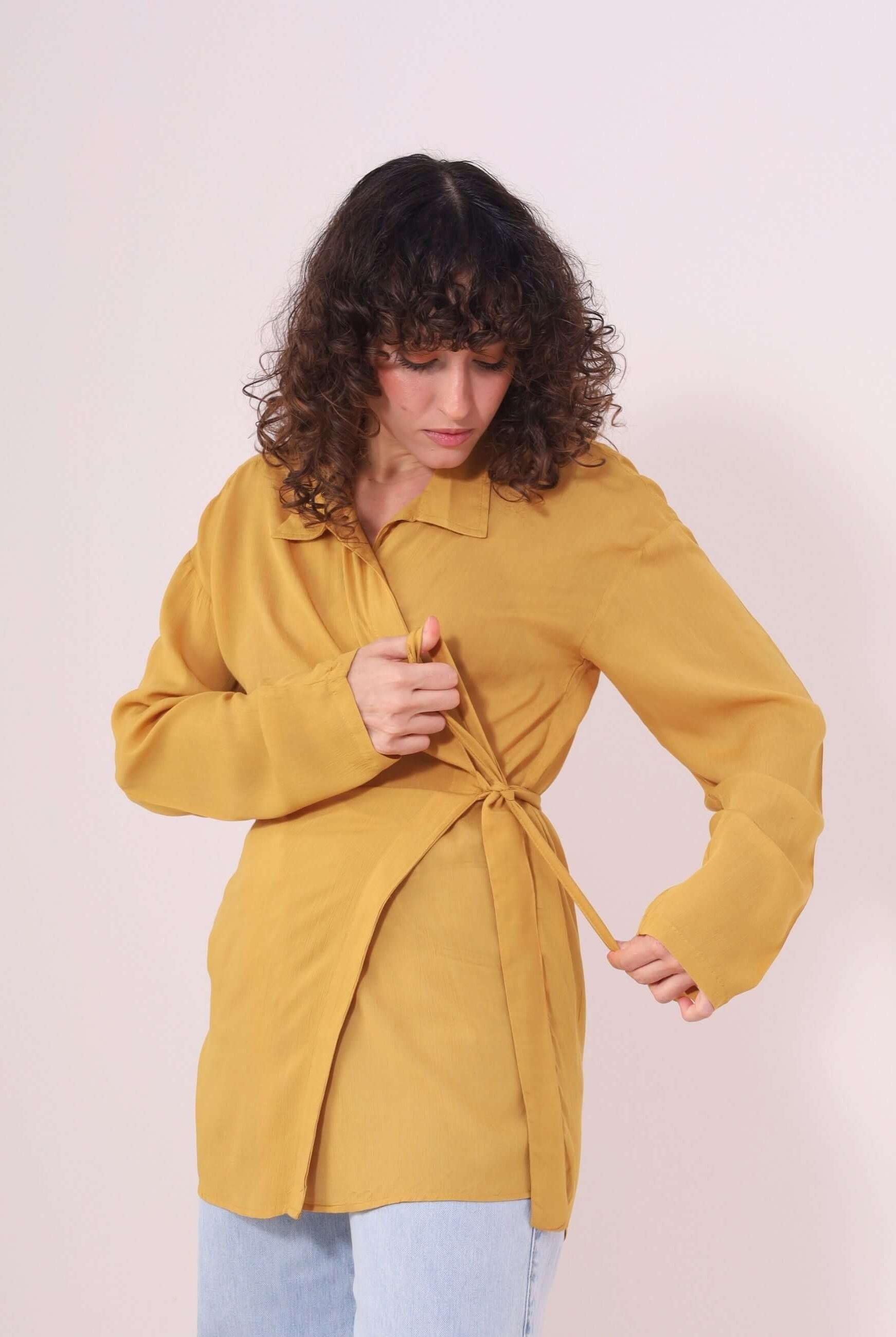Mulher vestindo Blusa Kalu Mostarda da Greenish em viscose, com faixa na cintura e gola retrô, ideal para looks descomplicados.