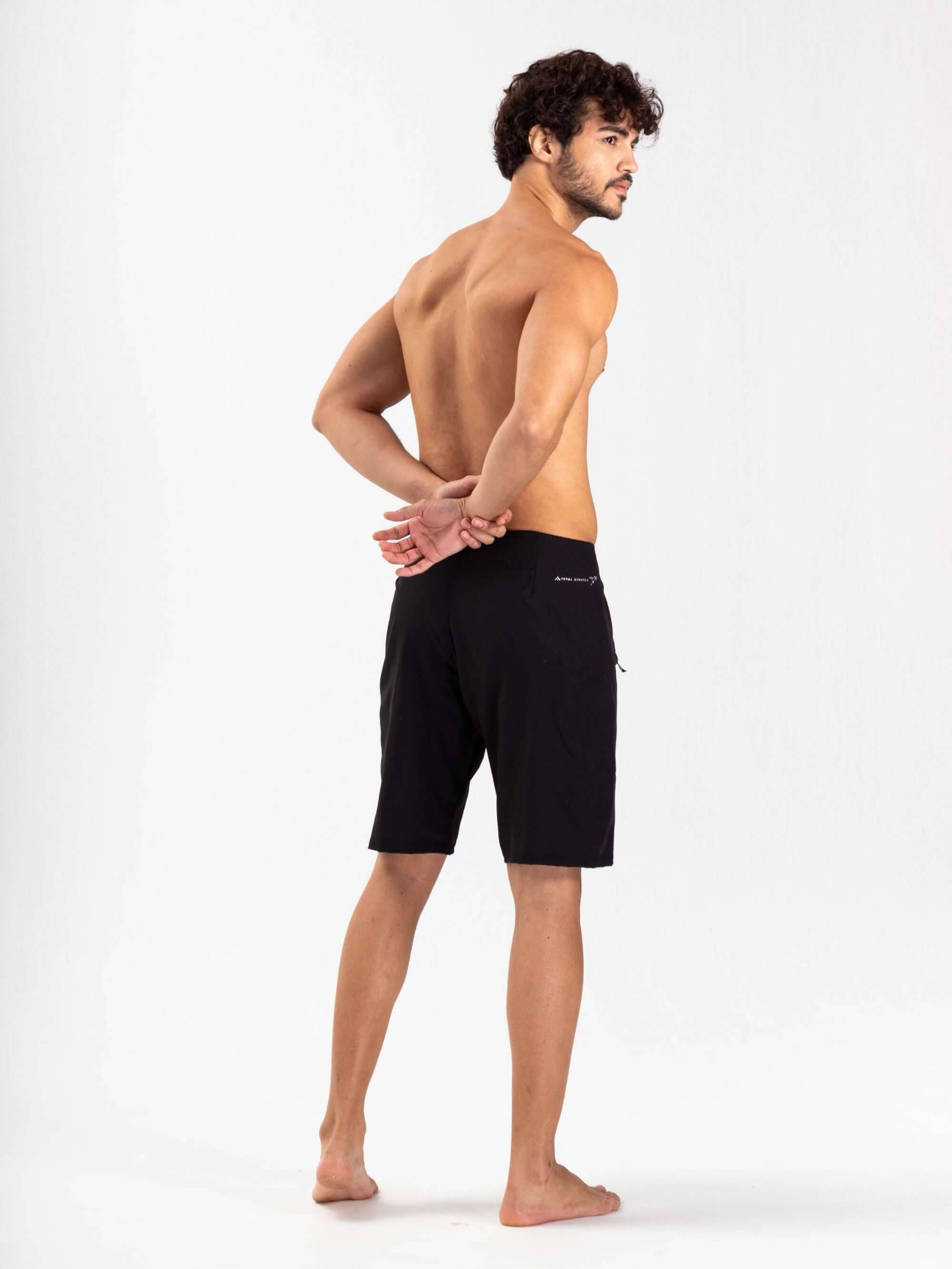 Modelo usando boardshort Total Stretch Preto da marca Greenish, mostrando a parte de trás da peça, ideal para alta performance no mar.