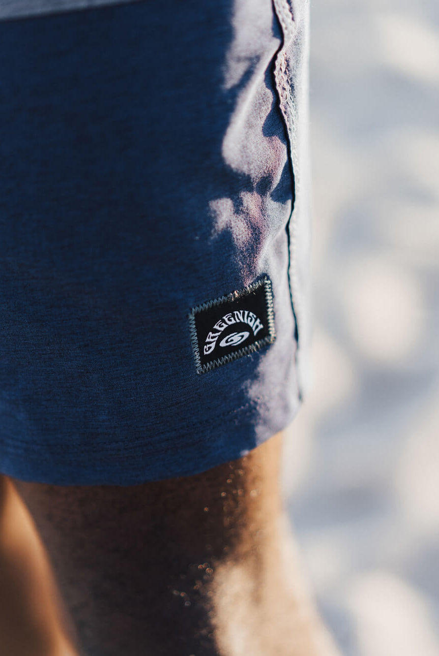 Detalhe da bermuda Boardwalk Three Panels da Greenish, mostrando a etiqueta em um ambiente de praia.