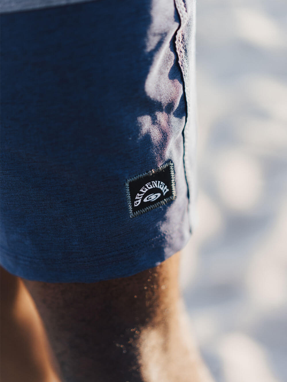 Detalhe da bermuda Boardwalk Three Panels da Greenish, mostrando a etiqueta em um ambiente de praia.