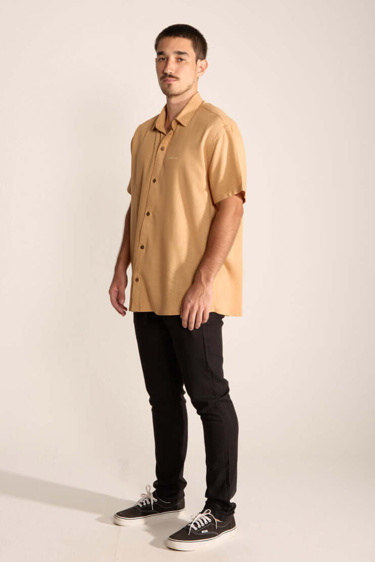 Imagem de homem usando camisa bege e calça preta, estilo casual, da marca Greenish.