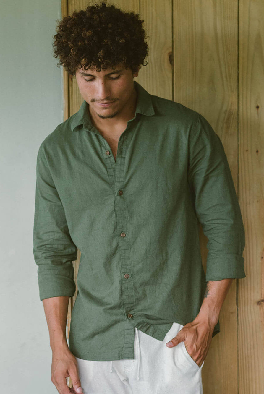 Homem usando camisa longa de linho verde da Greenish, com botões de coco, em cenário casual.
