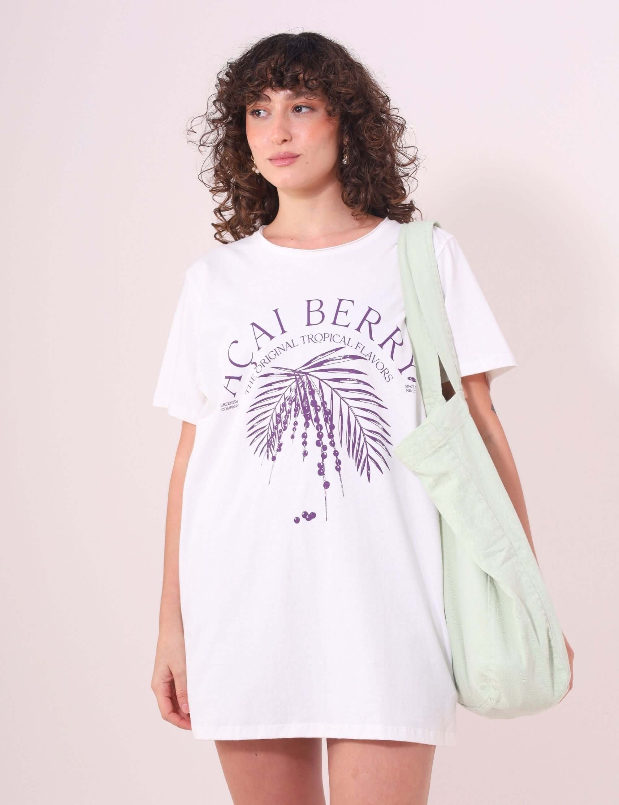 Mulher usando Camiseta Açai Berry em off white da marca Greenish, feita de algodão 100%, com estampa tropical roxa e modelagem ampla.