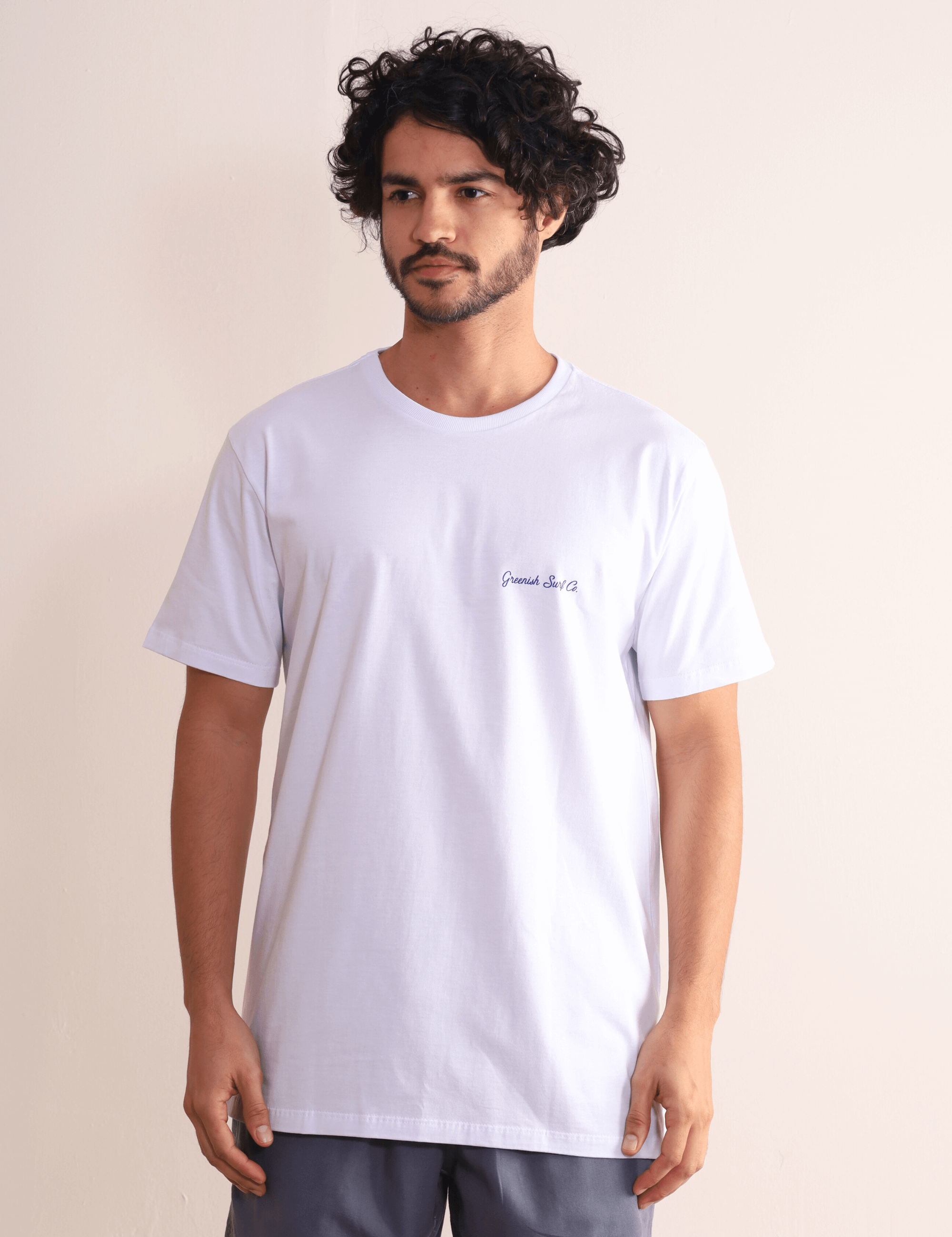 Homem vestindo camiseta branca Greenish Made By Surfers de algodão com estampa minimalista, ideal para uso diário e passeios na praia.