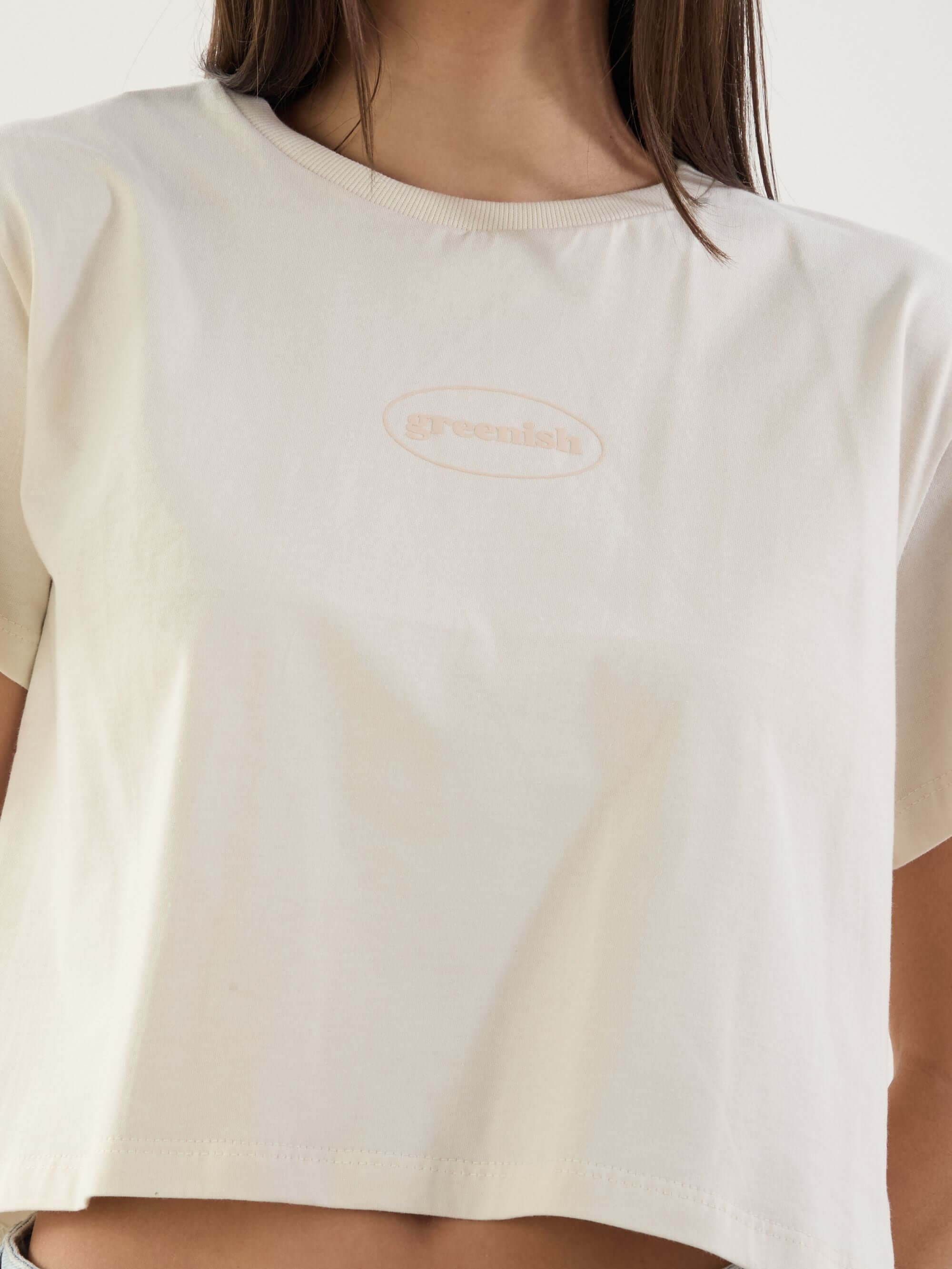 Camiseta cropped beige da marca Greenish, com logo em destaque, estilo moderno e confortável.