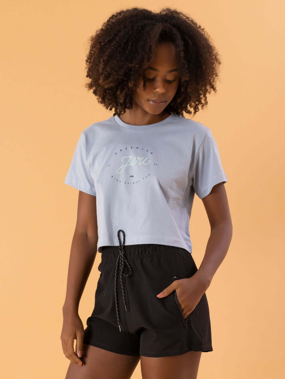 Camiseta cropped em azul claro com estampa, usada por modelo com cabelo cacheado, da marca Greenish.