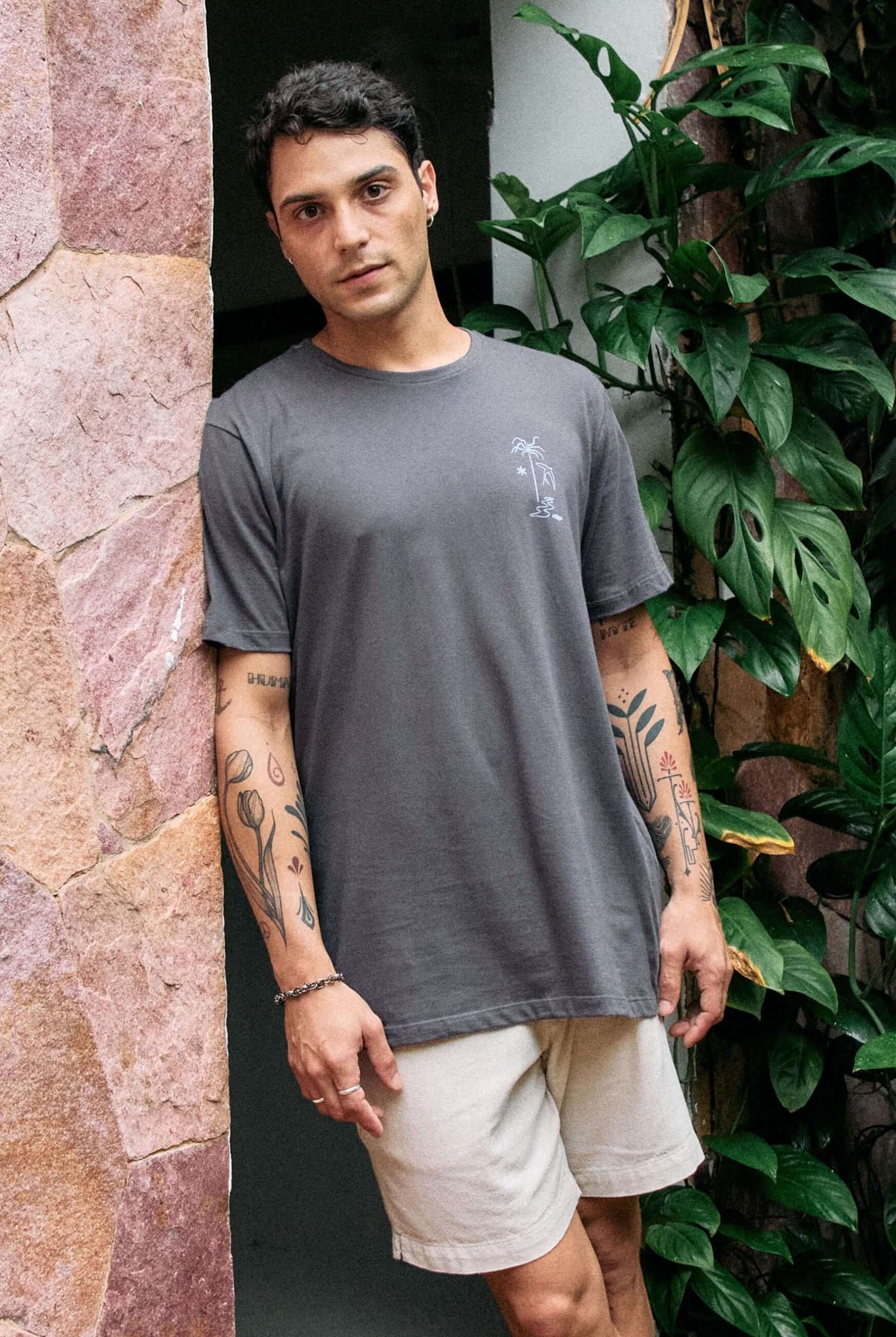 Homem vestindo camiseta Grafite da Greenish com estampa The Seed, The Sun and Moon em cenário natural com plantas.