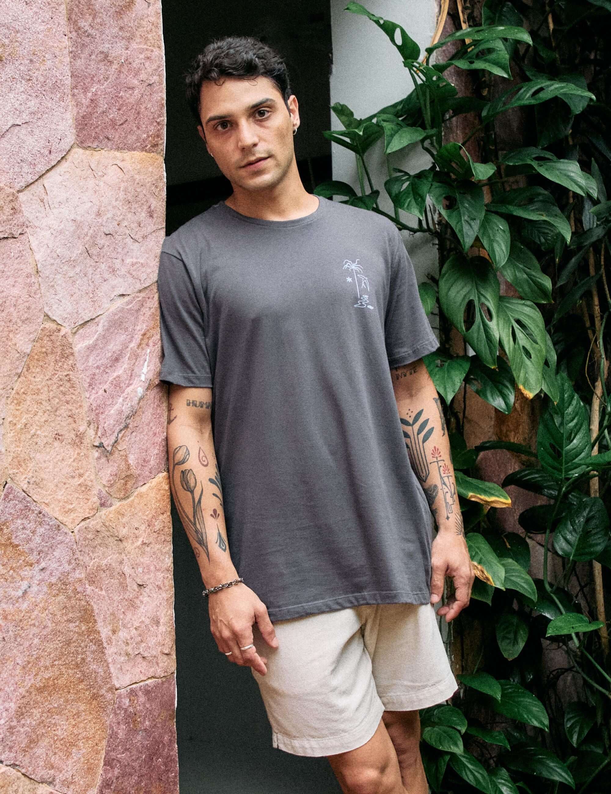 Homem vestindo camiseta Grafite da Greenish com estampa The Seed, The Sun and Moon em cenário natural com plantas.