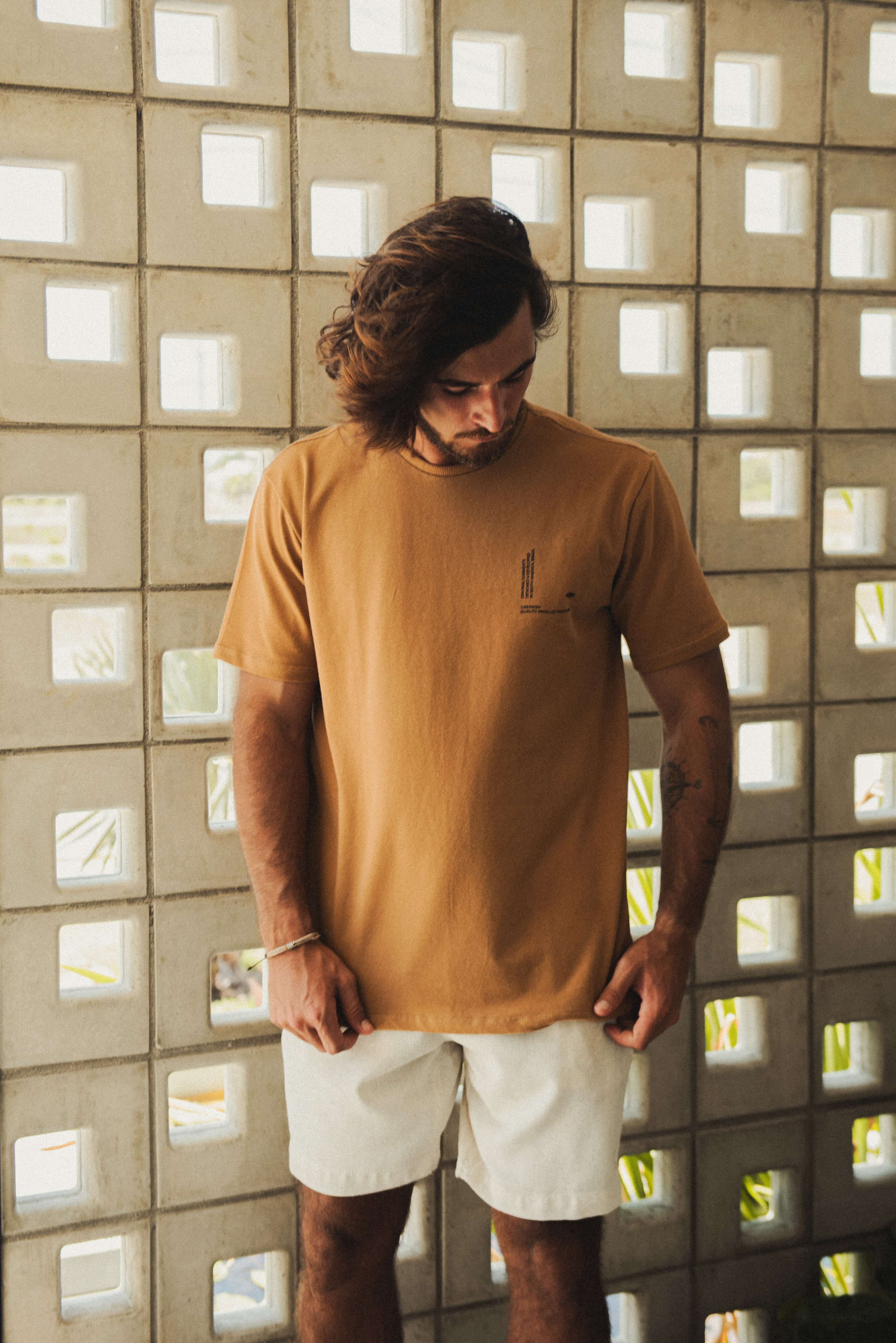 Modelo veste Camiseta Greenish Quality Product - Caqui em cenário casual, destacando design minimalista e conforto diário.