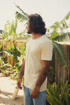 Homem vestindo CAMISETA STONE RAWEDGE - AREIA da marca Greenish, em ambiente tropical. Camiseta masculina de algodão com visual raw chic.