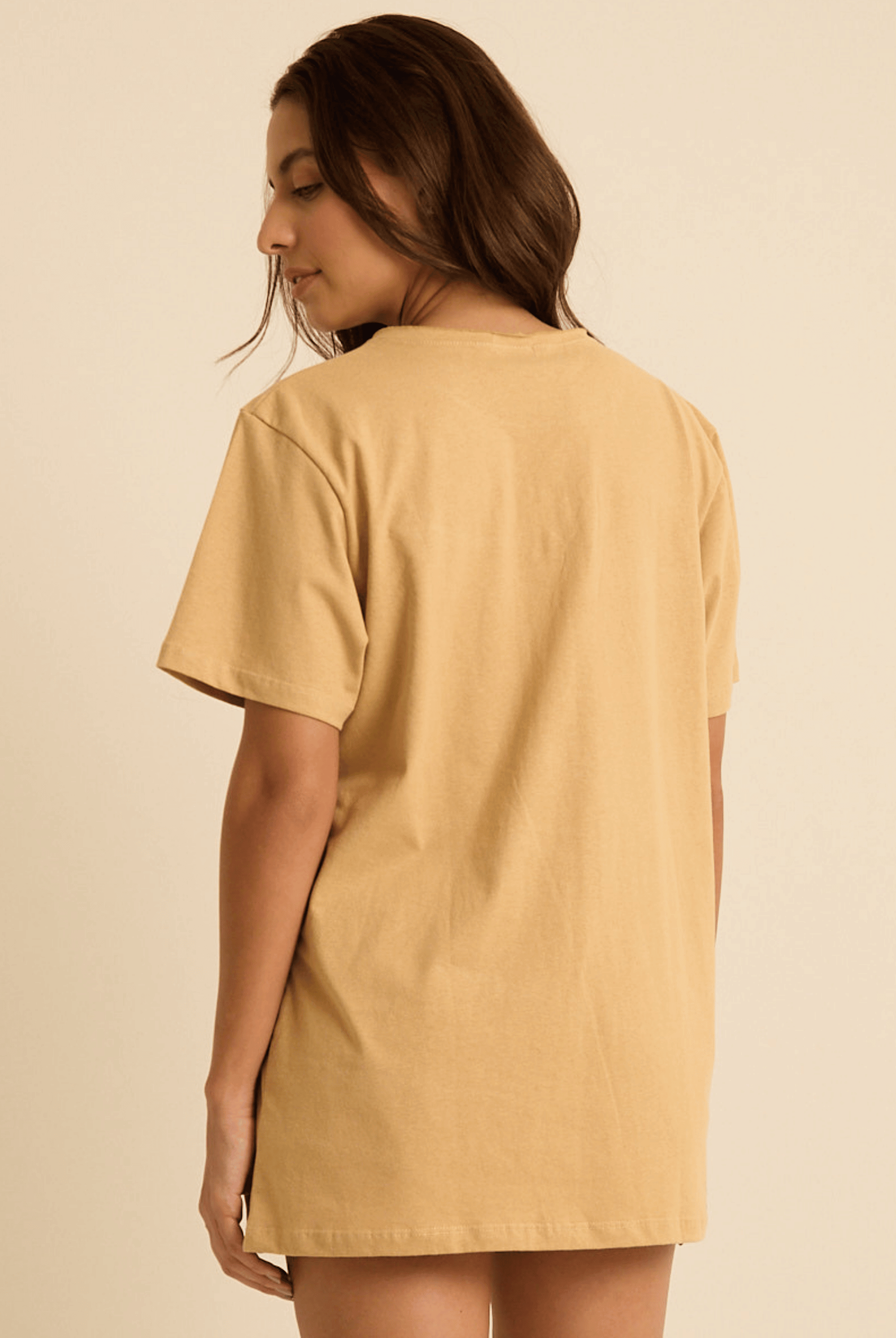 Modelo feminina usando camiseta oversized Siriguela bege da marca Greenish, vista de trás, em tecido 100% algodão.