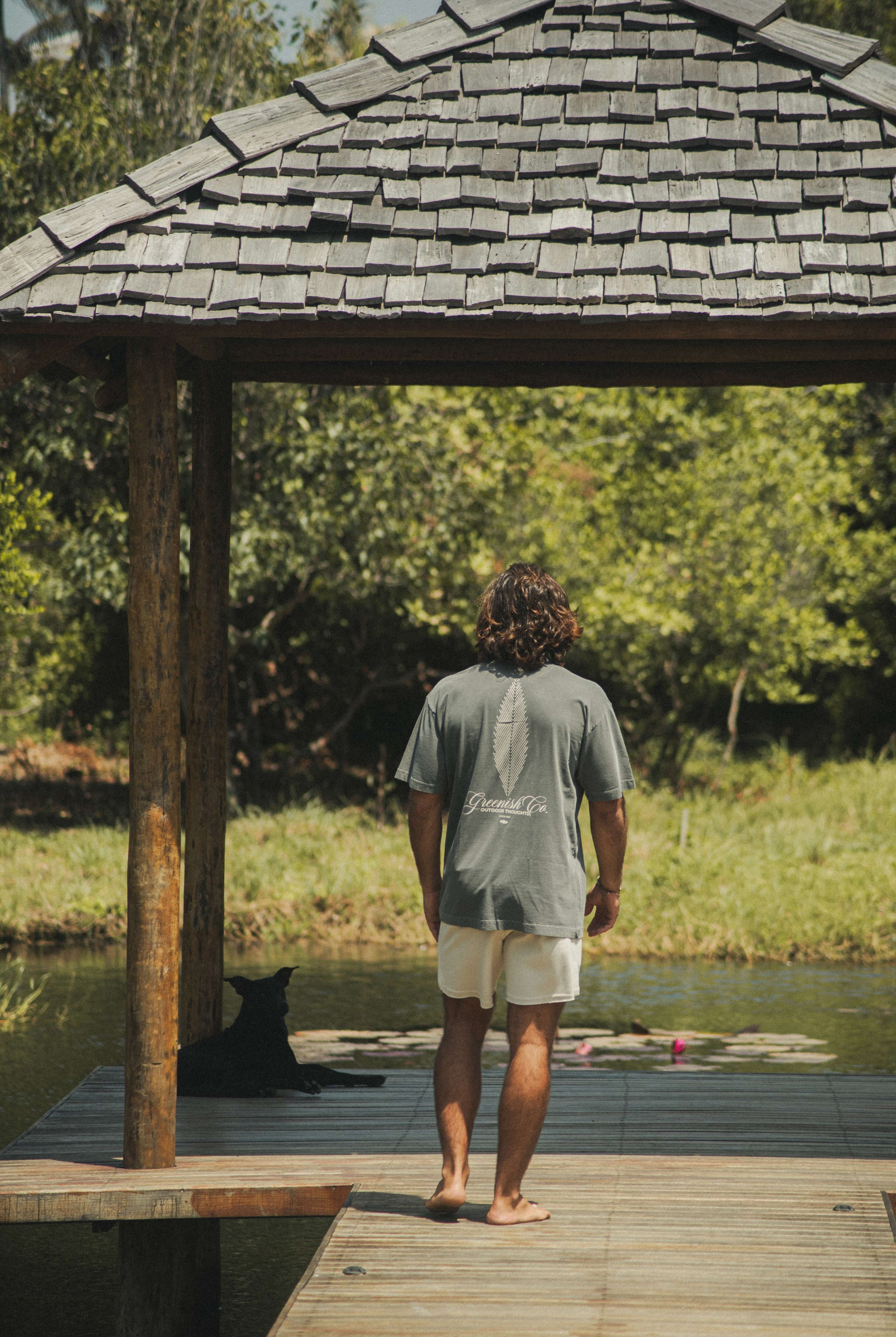 Homem em deck usando Camiseta Oversized Stong Leaf Plank - Chumbo da Greenish, destacando estampa de folha e logo, em cenário natural.
