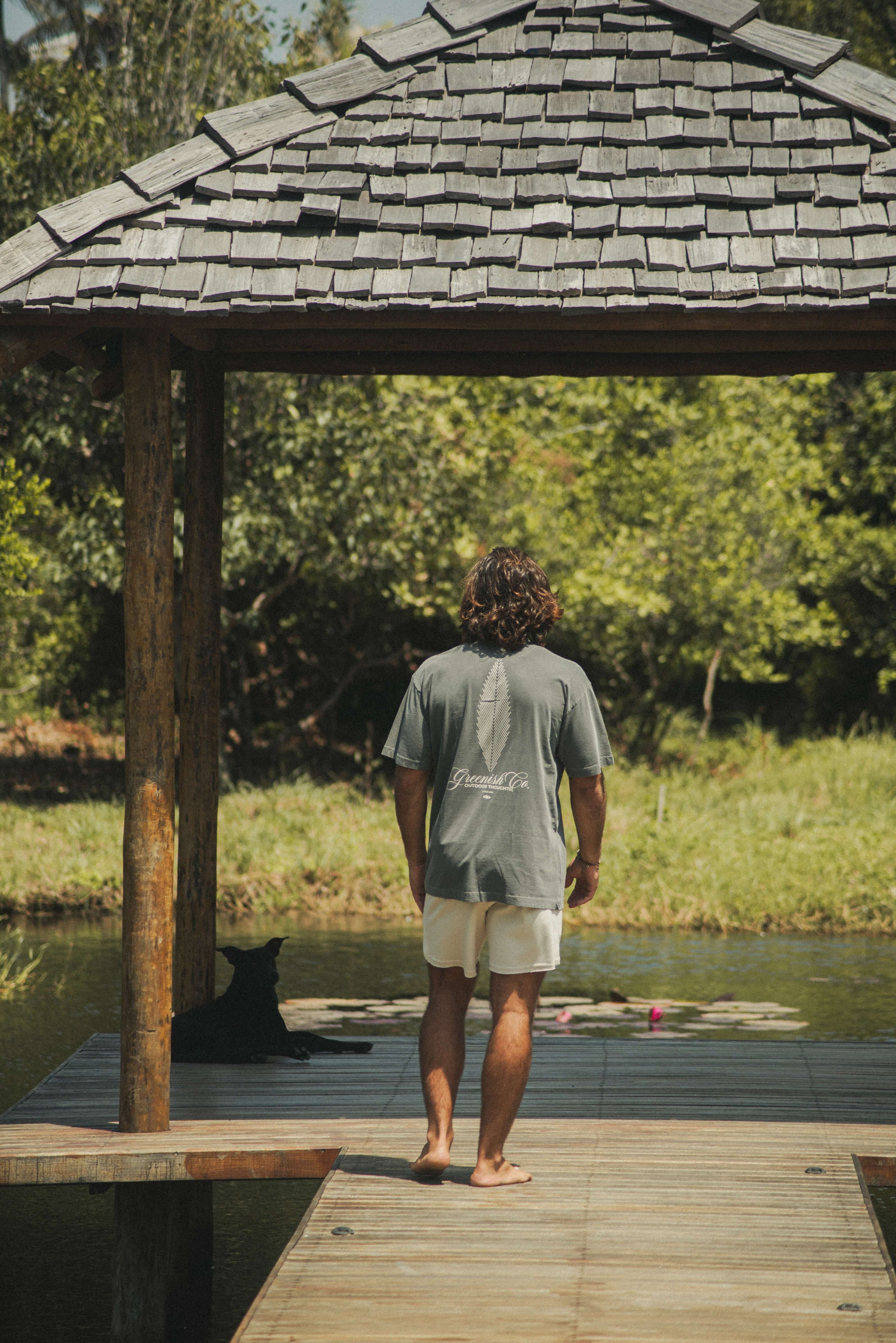 Homem em deck usando Camiseta Oversized Stong Leaf Plank - Chumbo da Greenish, destacando estampa de folha e logo, em cenário natural.