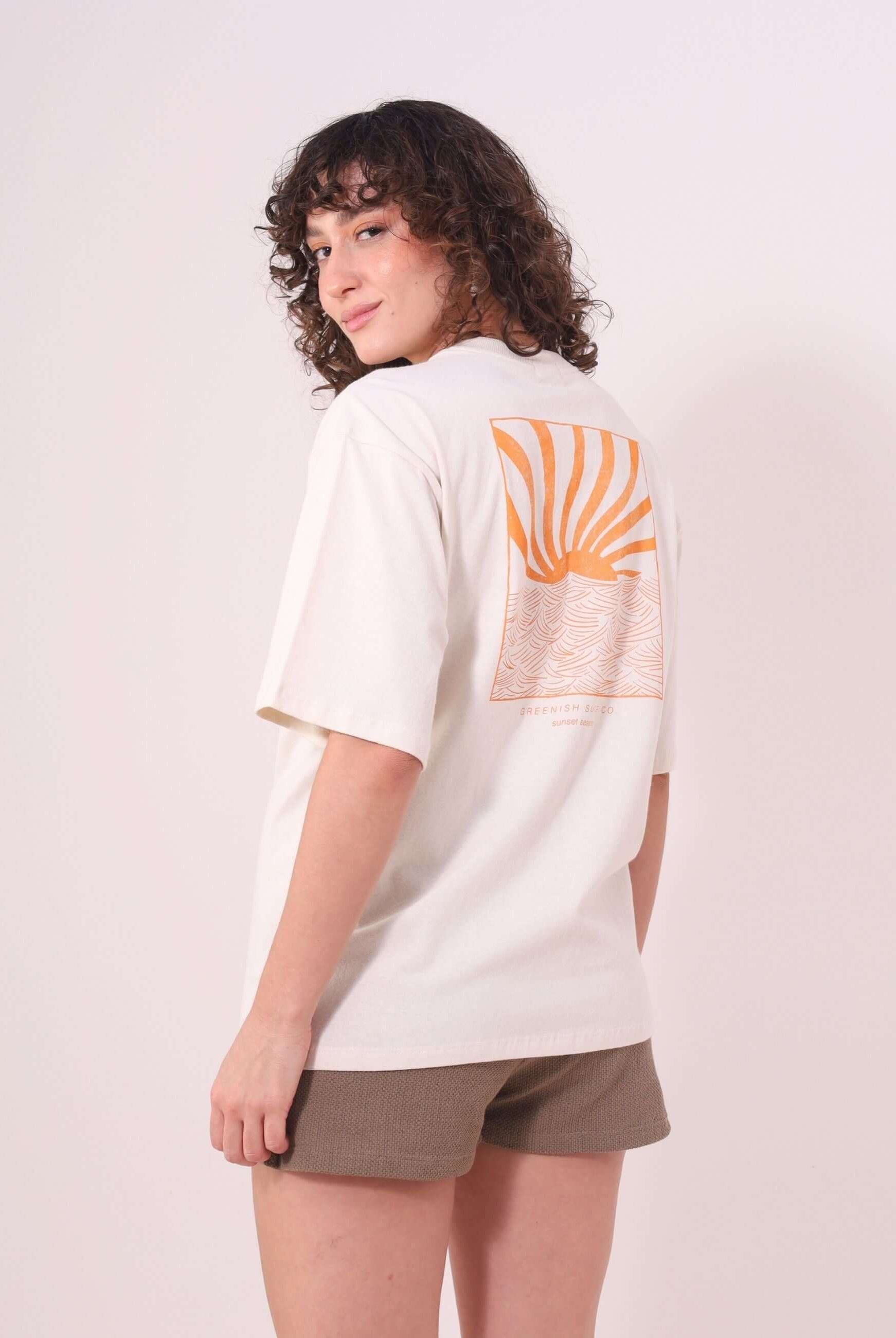Mulher vestindo Camiseta Oversized Sunset Session - Natural da Greenish, com estampa de ondas e pôr do sol, em um look casual.