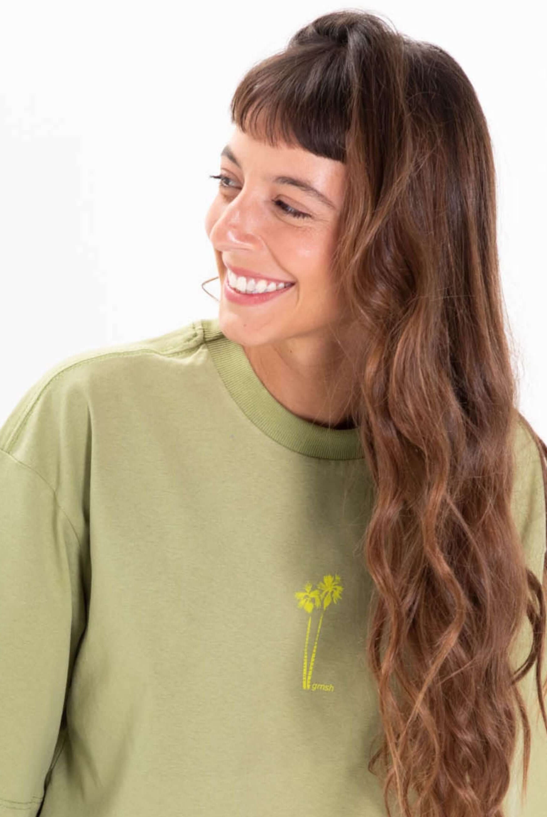 Camiseta oversized verde com estampa de palmeiras da Greenish, modelo feminino sorrindo.