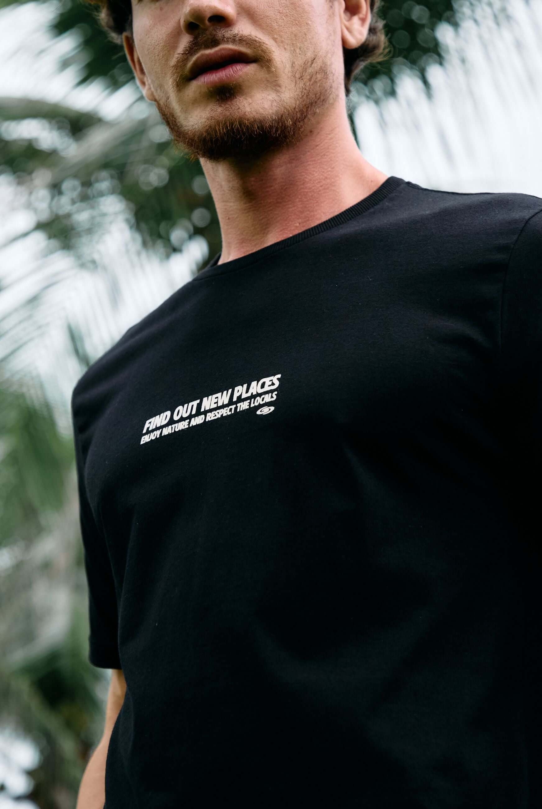 Homem vestindo camiseta preta Seagull Greenish com estampa, em meio à natureza tropical, representando liberdade e estilo.
