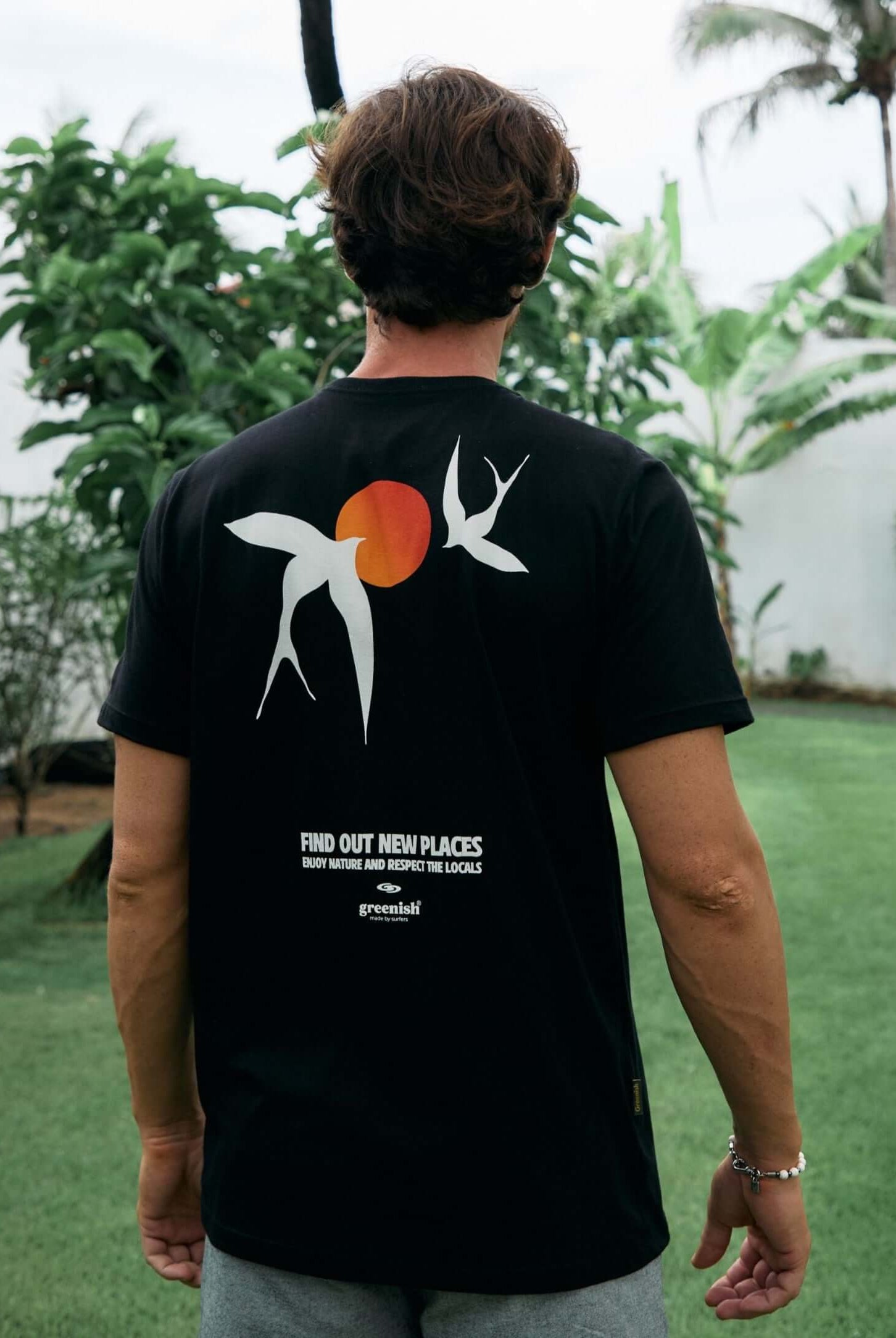 Homem usando a Camiseta Seagull preta da Greenish com arte inspirada em gaivotas e sol, em ambiente natural ao ar livre.